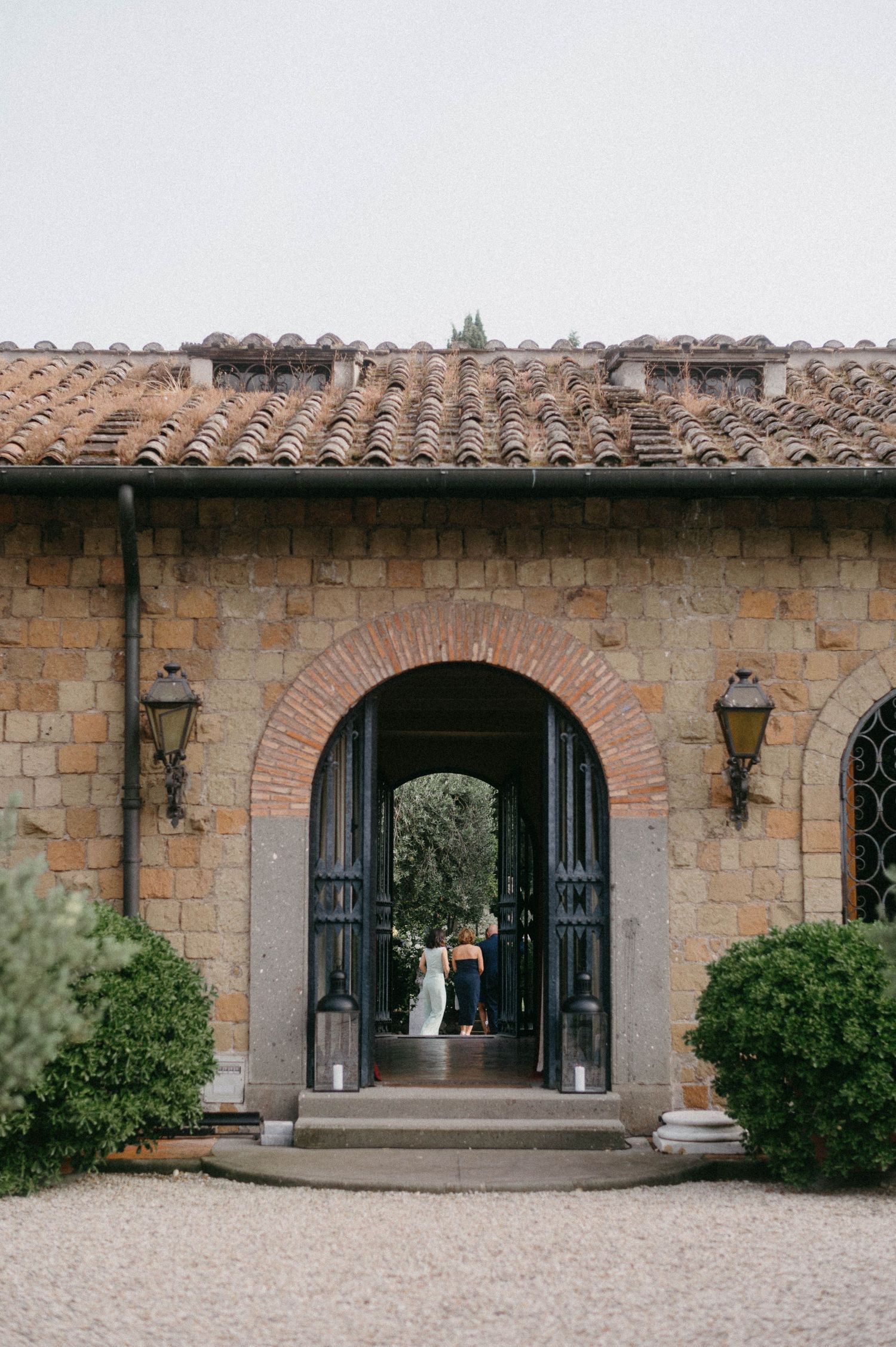 Stone archway entrance to Italian villa with greenery and gravel path.