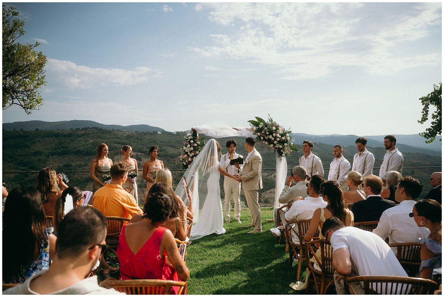 Outdoor mountain wedding ceremony takes place on a hilltop overlooking a scenic valley on a bright sunny day.