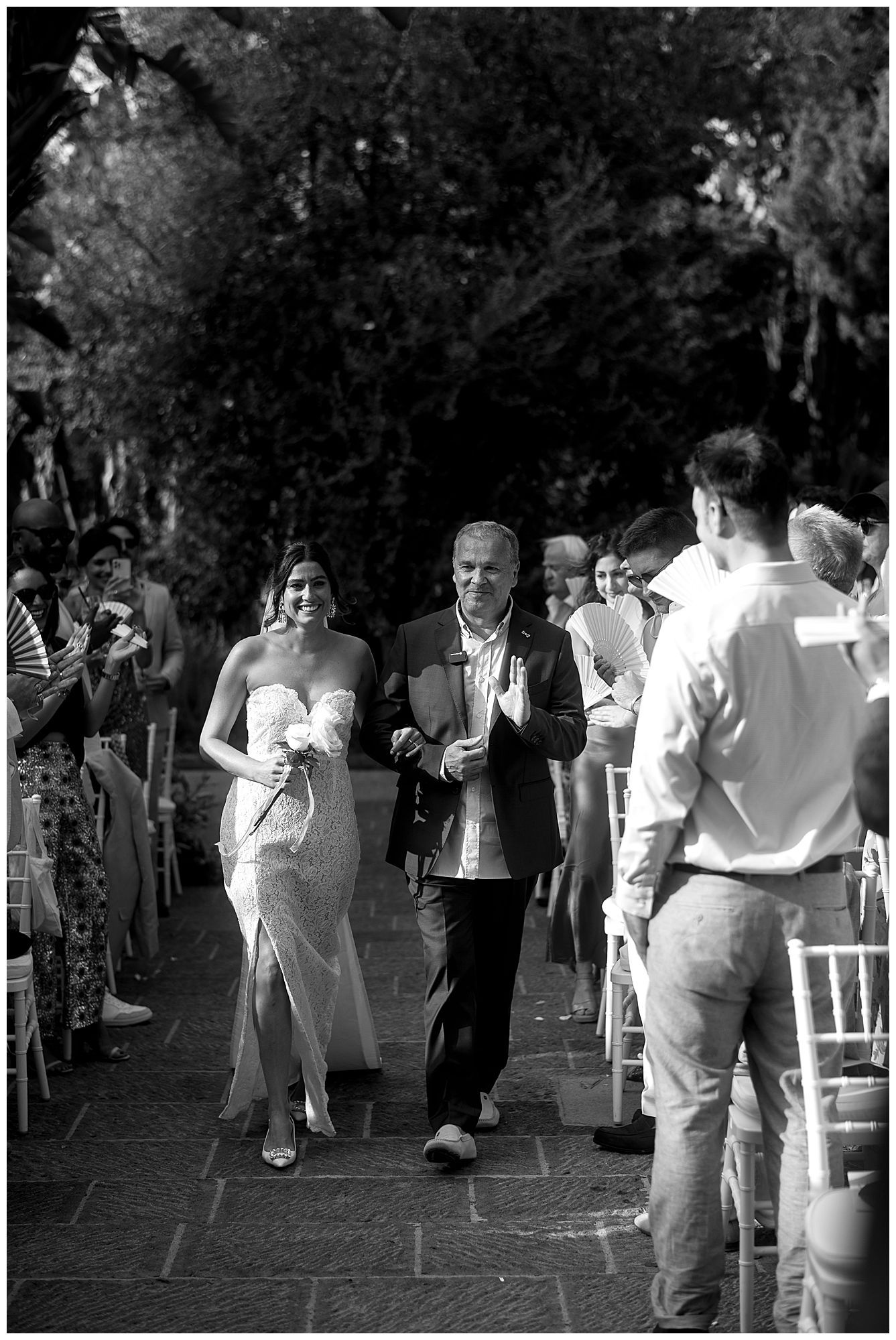 A black and white photograph of a wedding reception entrance with guests walking down a stone pathway outdoors.