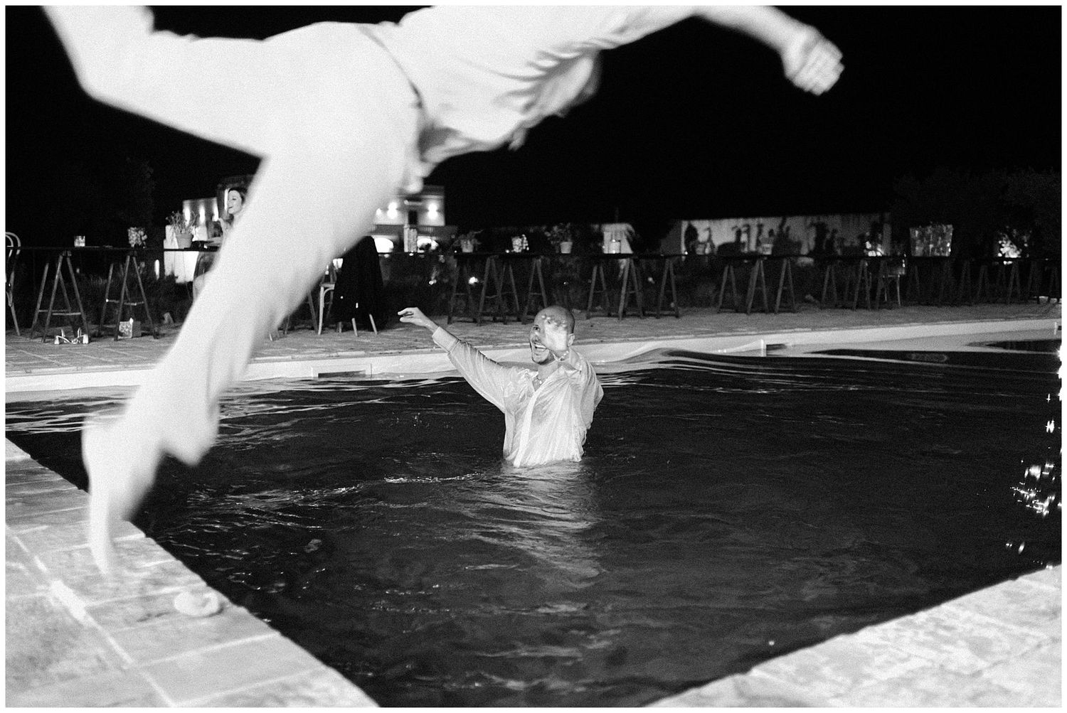 Black and white photo of swimmers in a pool creating splashes during a nighttime swim performance.