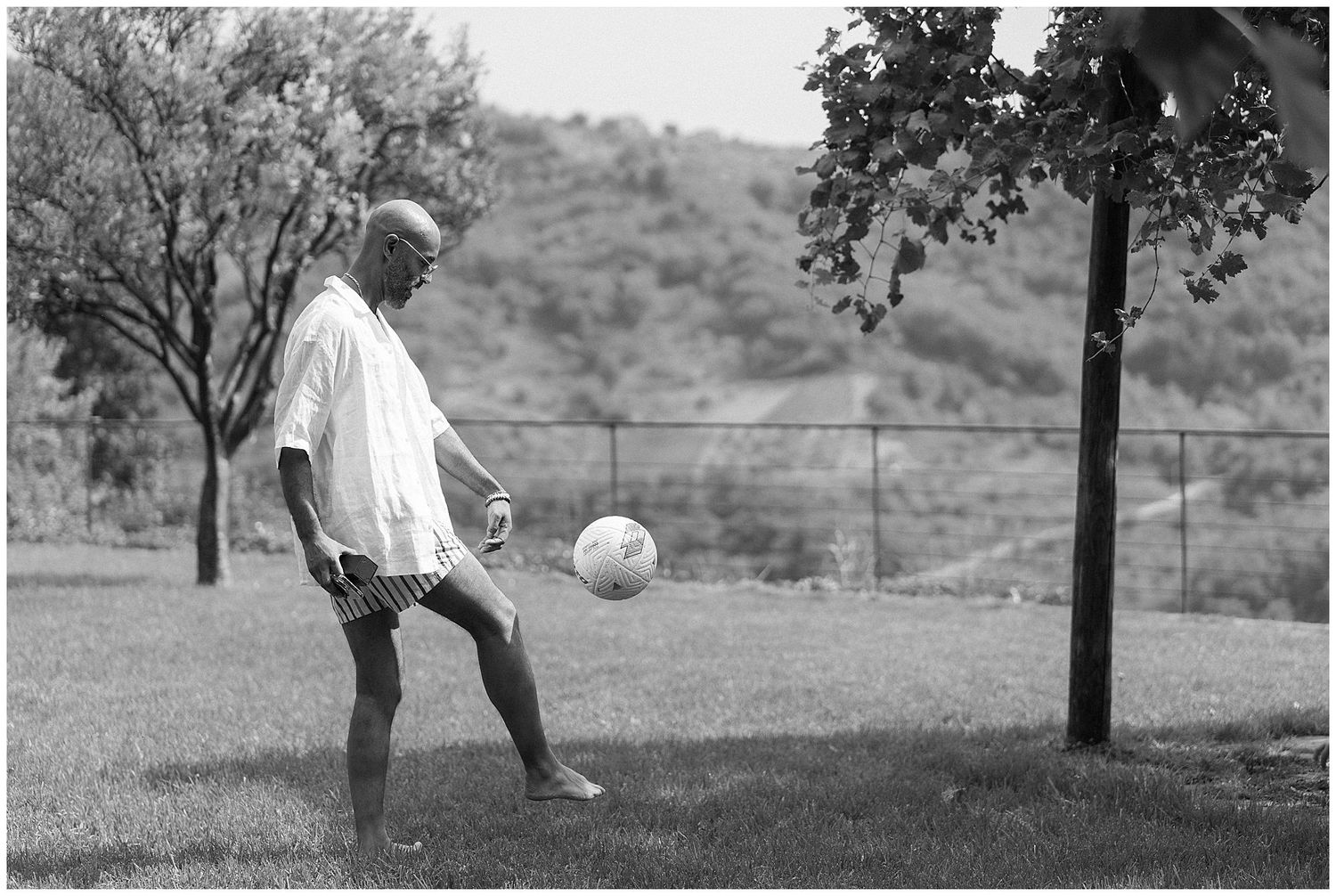 A person plays with a soccer ball on a grassy hill in a black and white photograph.