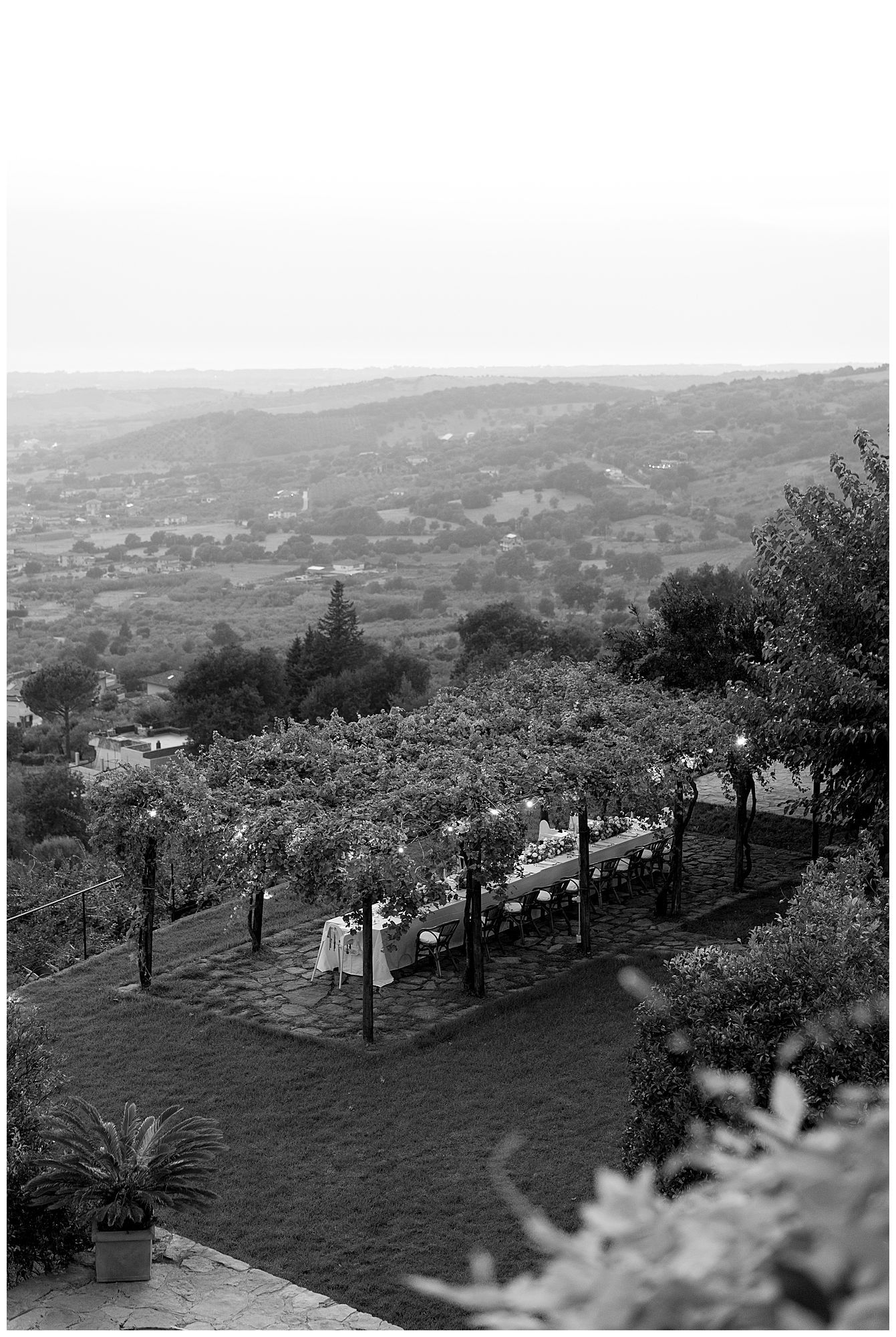 A black and white vintage photograph shows people gathered in a garden overlooking a hillside landscape.