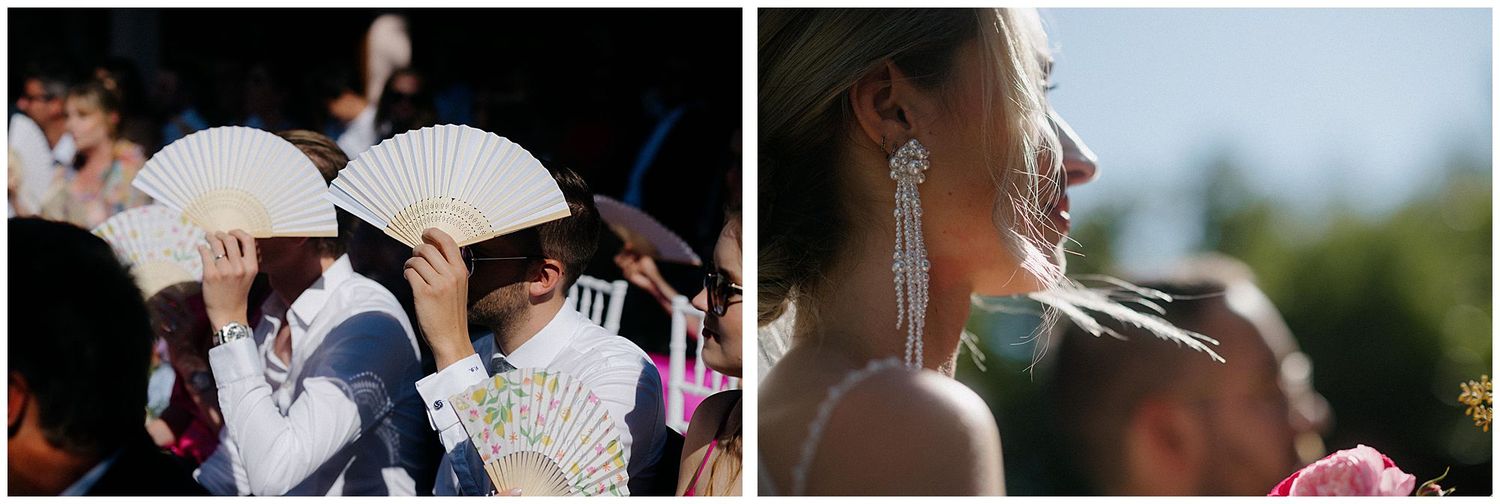 A couple kisses passionately while other wedding guests hold paper fans on a bright sunny day outdoors.