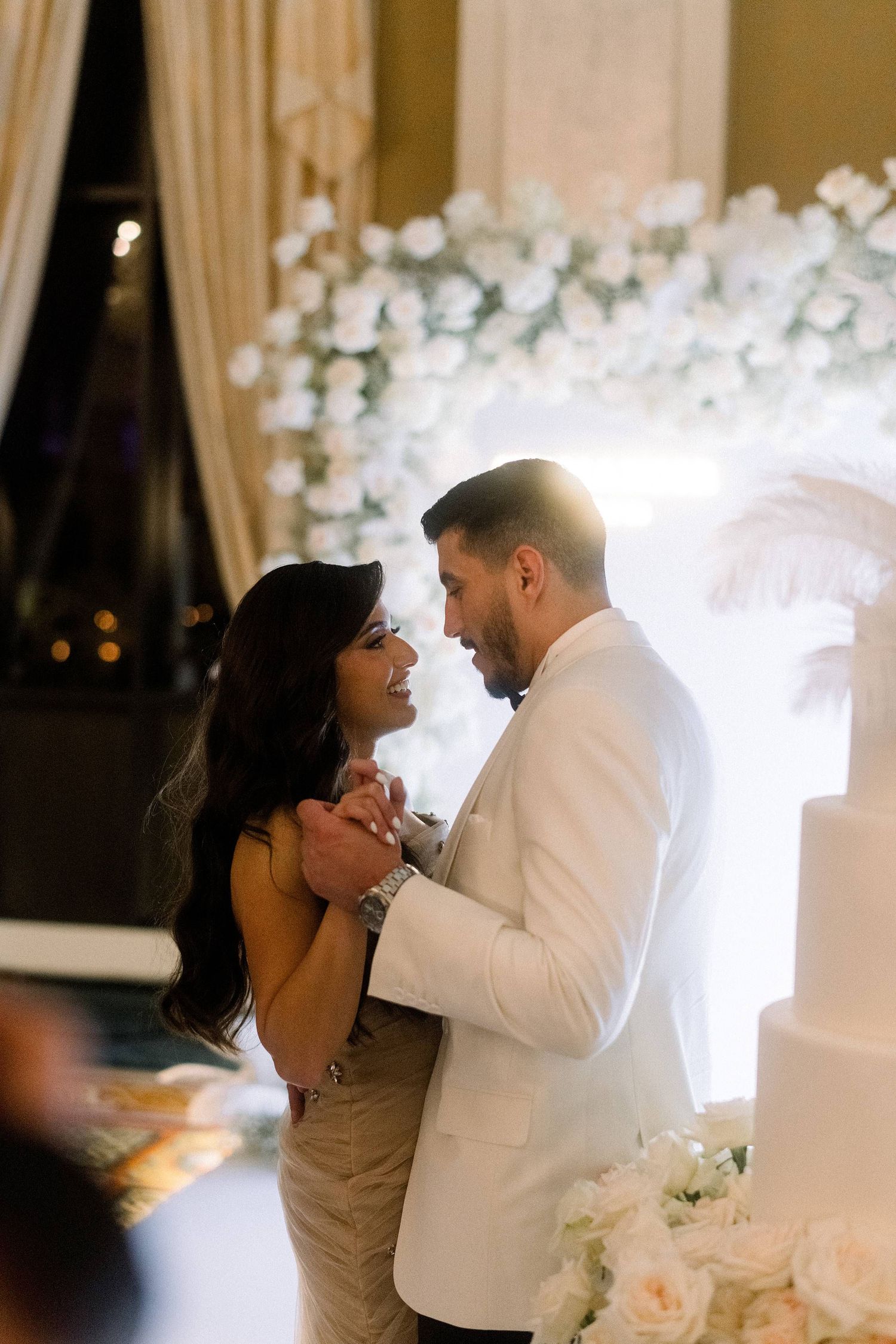 A romantic couple shares their first dance at a wedding reception with white floral decorations in the background.