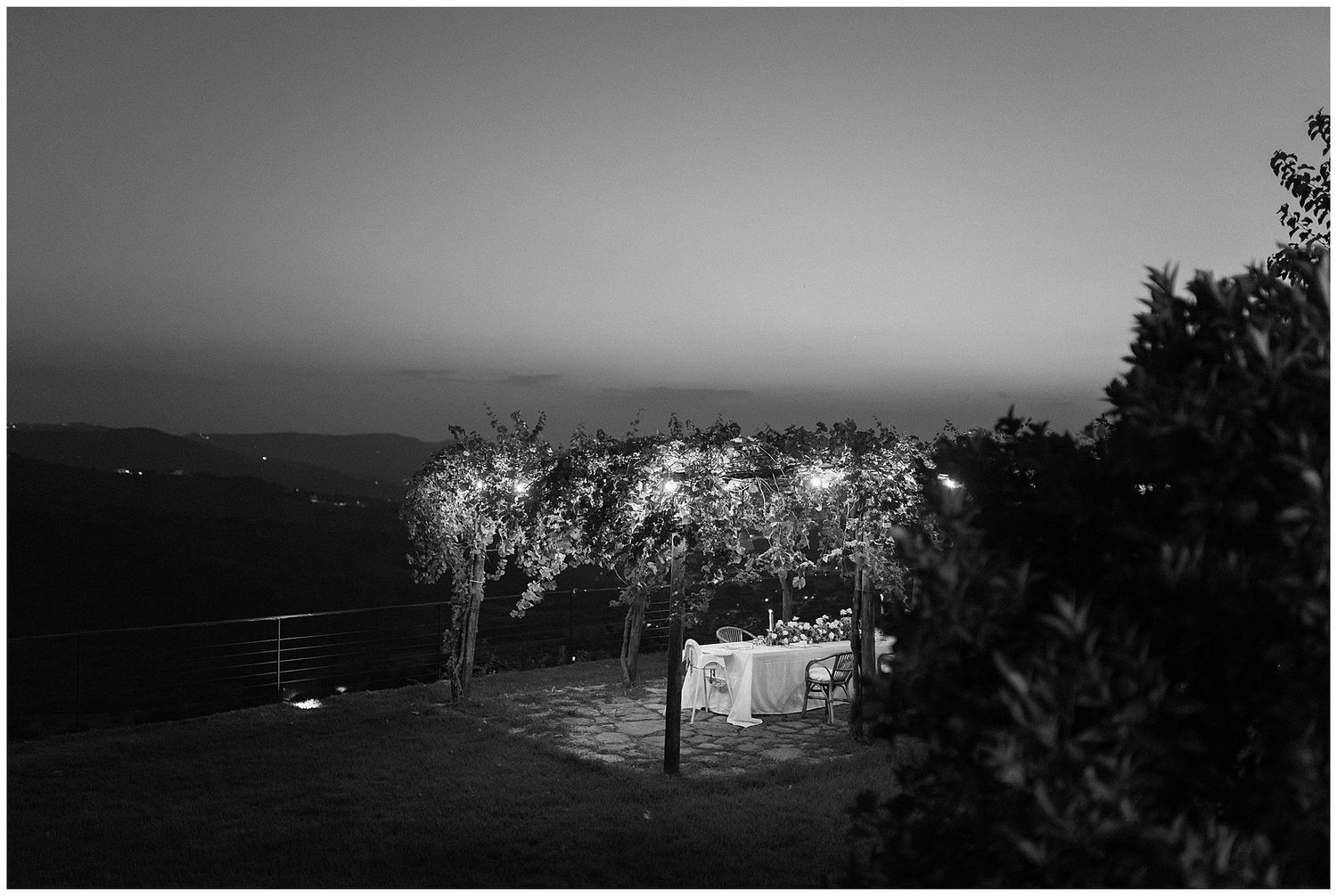 A monochrome night view shows illuminated trees glowing above a small caravan in a rural landscape.