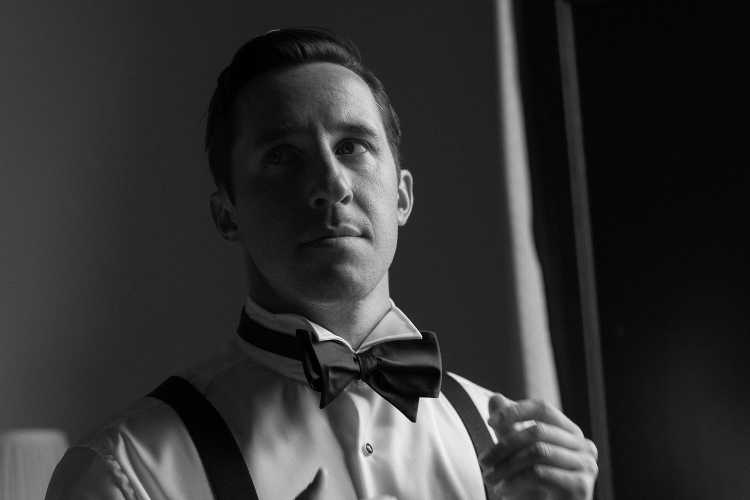 Black and white portrait of a person in formal attire with bowtie and suspenders looking to the side.