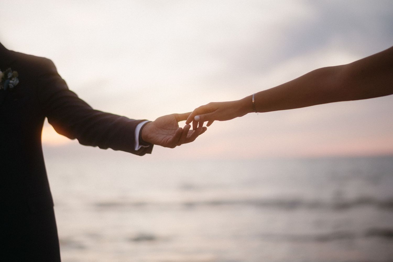 Silhouetted couple holding hands against blurred ocean sunset background creating romantic atmosphere.