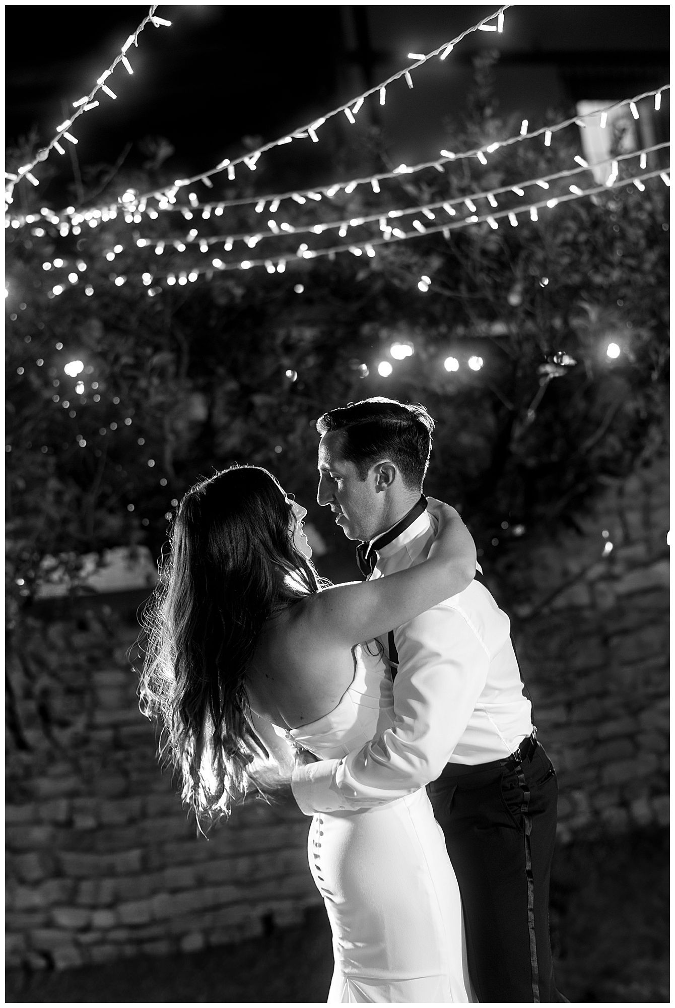 Newlyweds share a romantic dance under twinkling string lights at an outdoor evening reception.