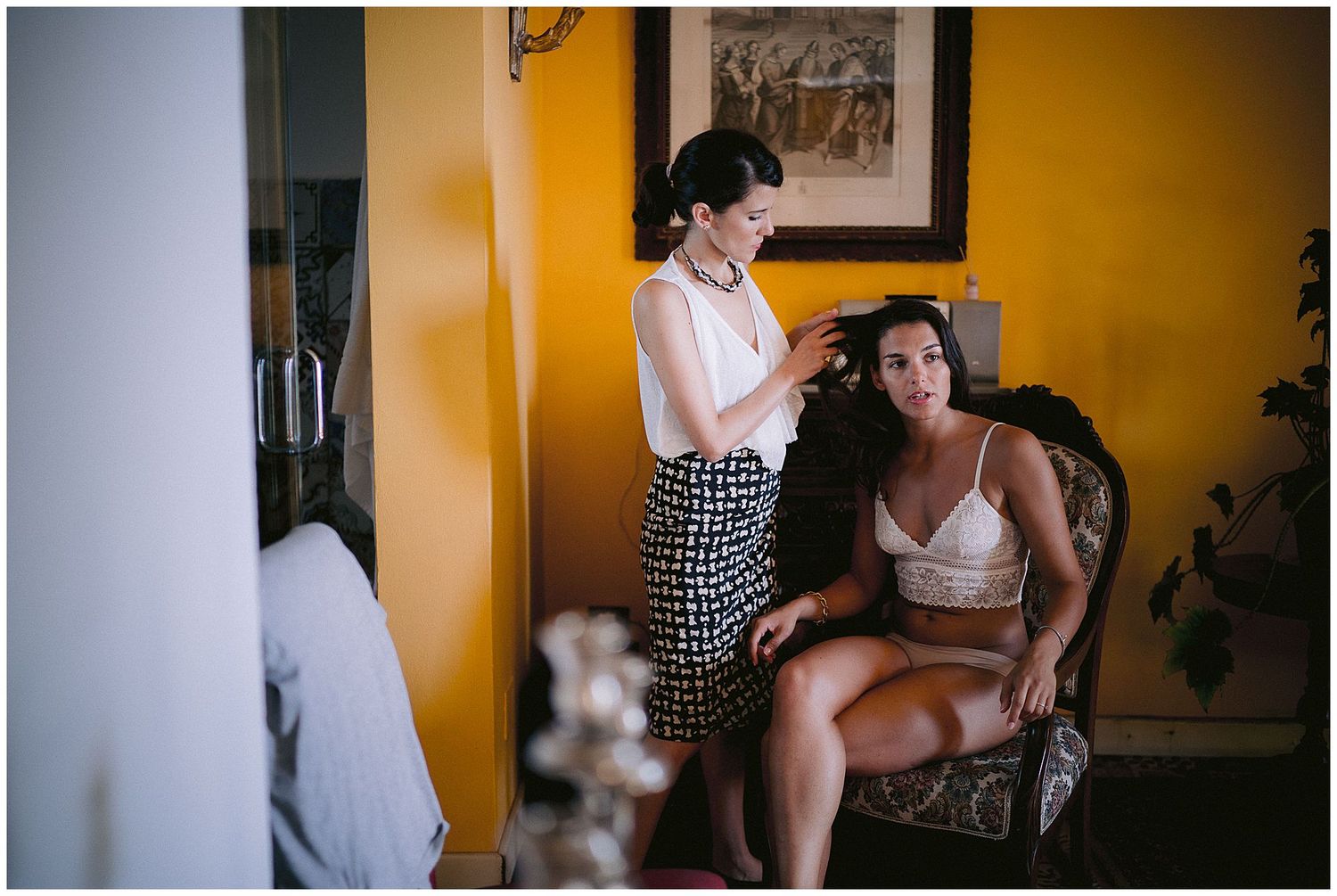 Two people in a room with yellow walls and a brown leather chair prepare for an intimate moment.