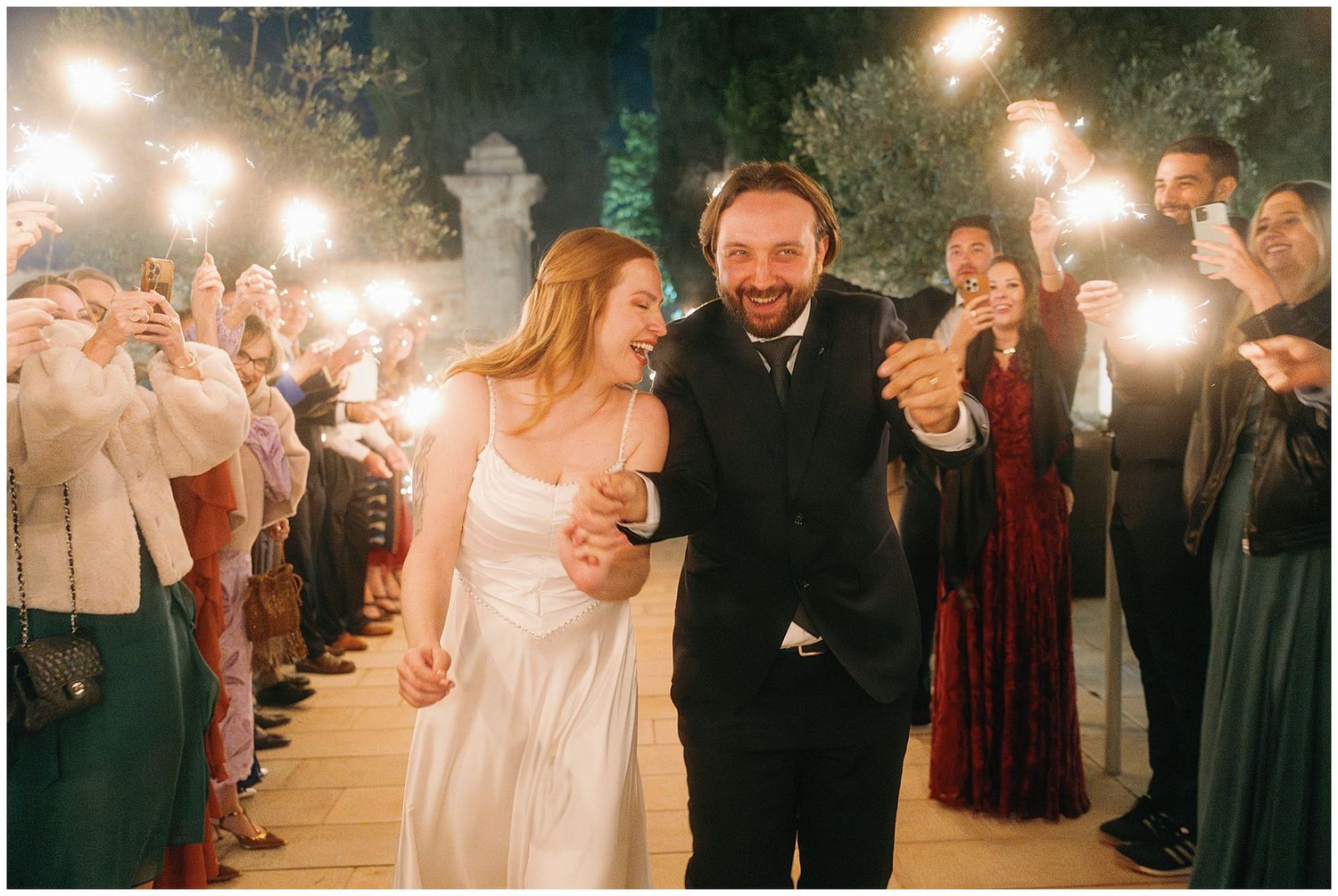 Newlyweds walk through their sparkler exit during nighttime wedding celebration with guests lining the path.