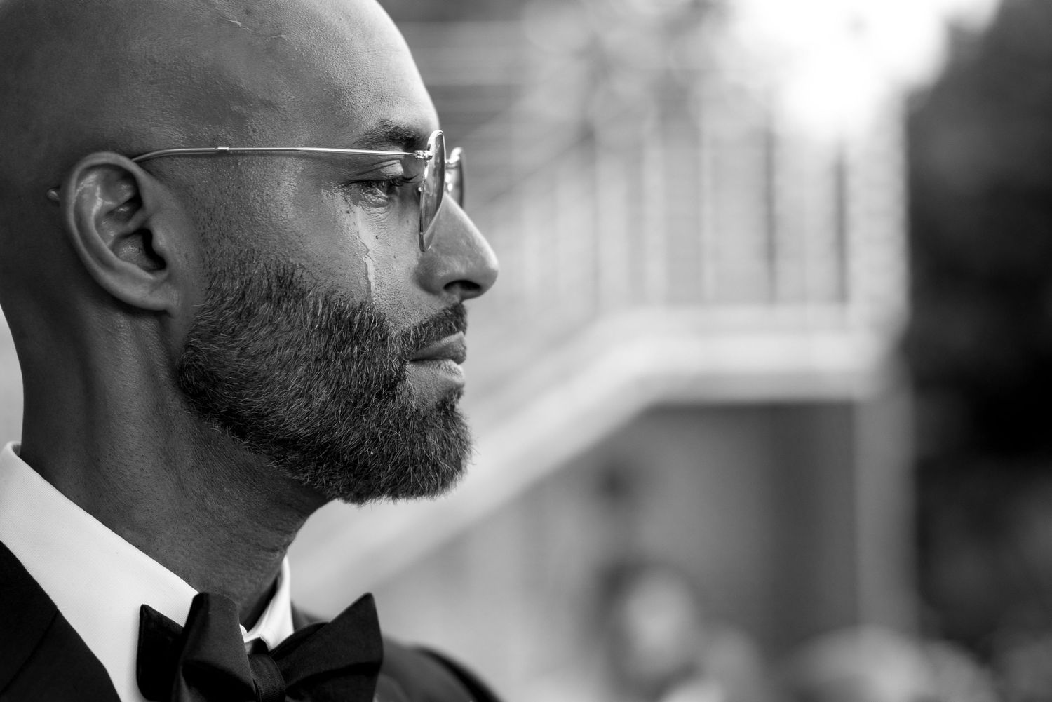 Side profile portrait of a man in formal black tie attire with glasses and beard.