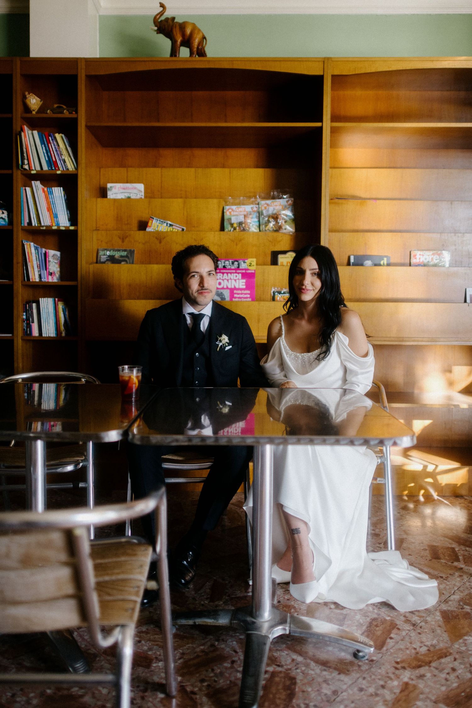 Newlyweds sit together at bar with wooden shelving and vintage decor.
