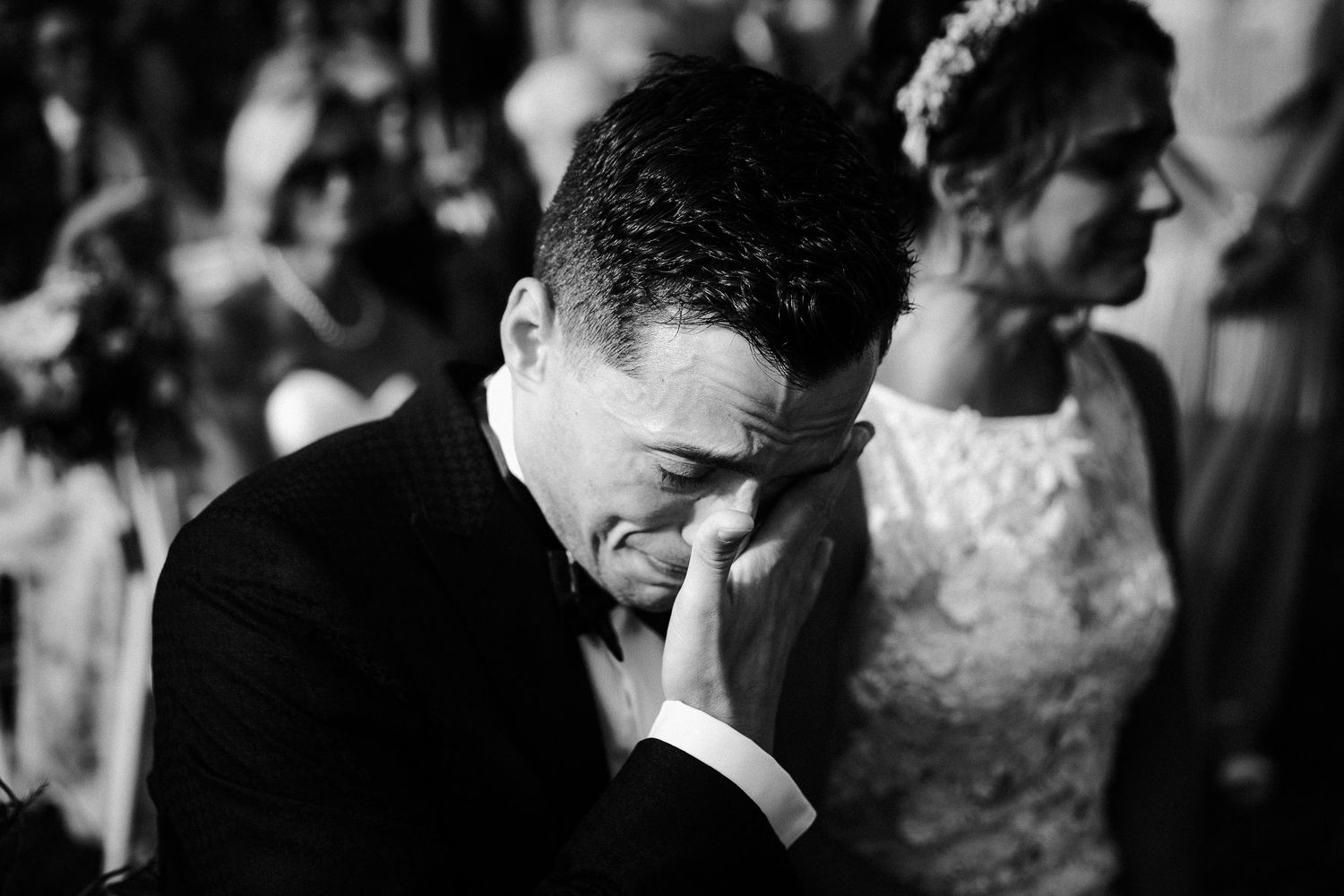 Black and white photo of someone wiping tears during an emotional wedding moment.