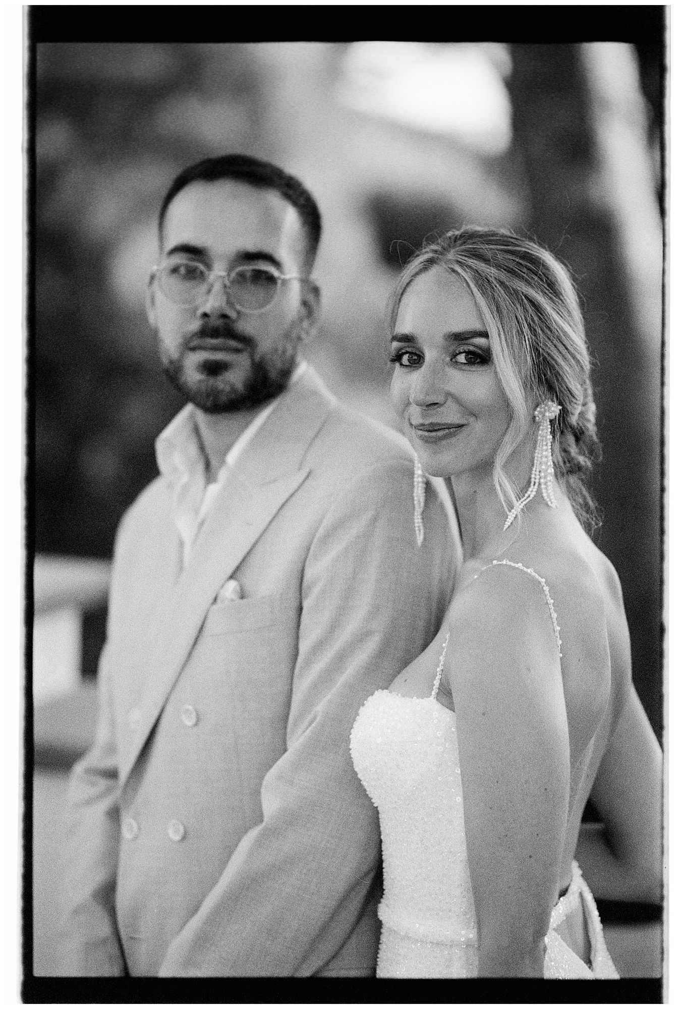 A black and white wedding portrait showing a couple in a bridal gown and light colored suit.