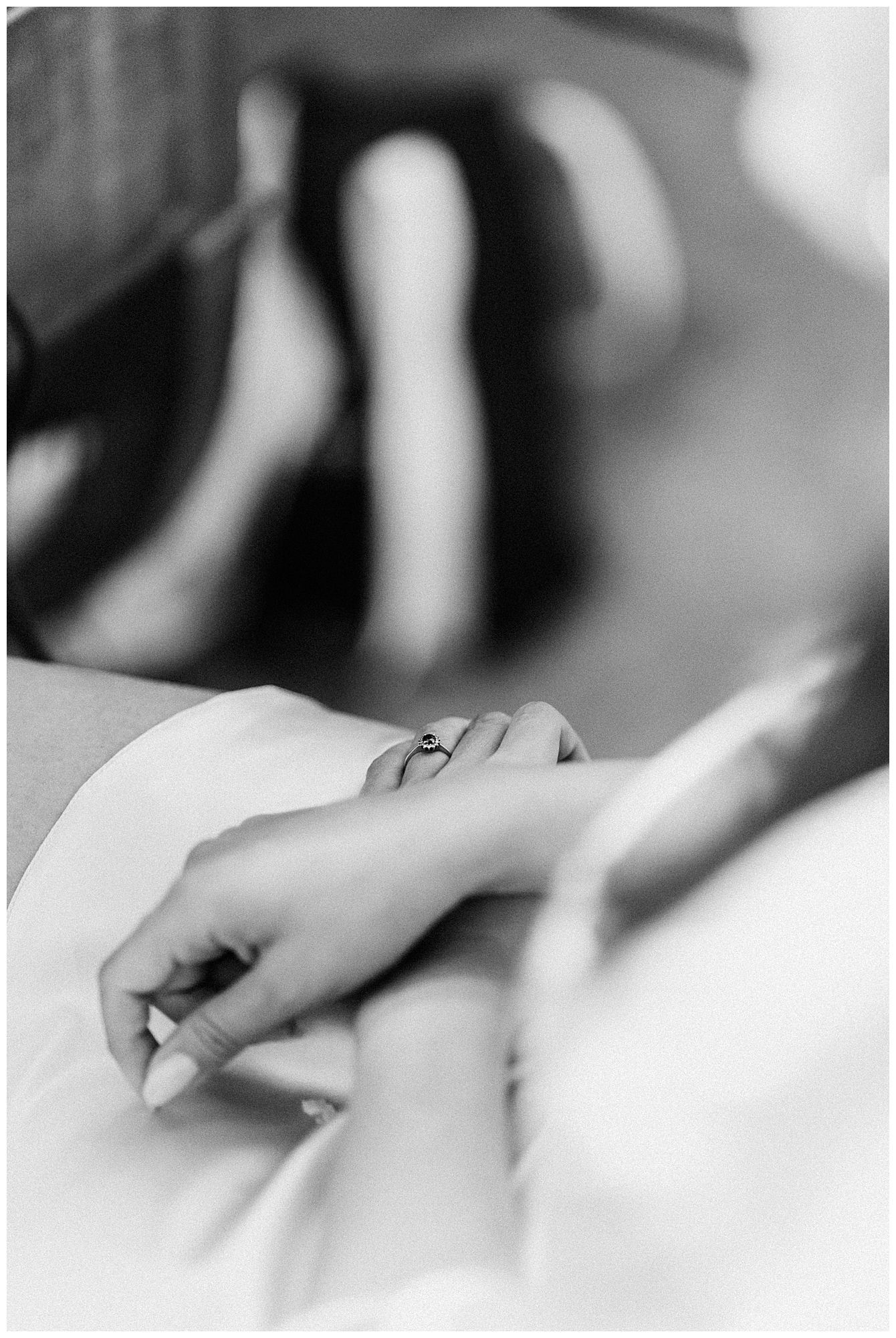 A close-up black and white photograph shows a hand writing or drawing on paper with soft focus in the background.