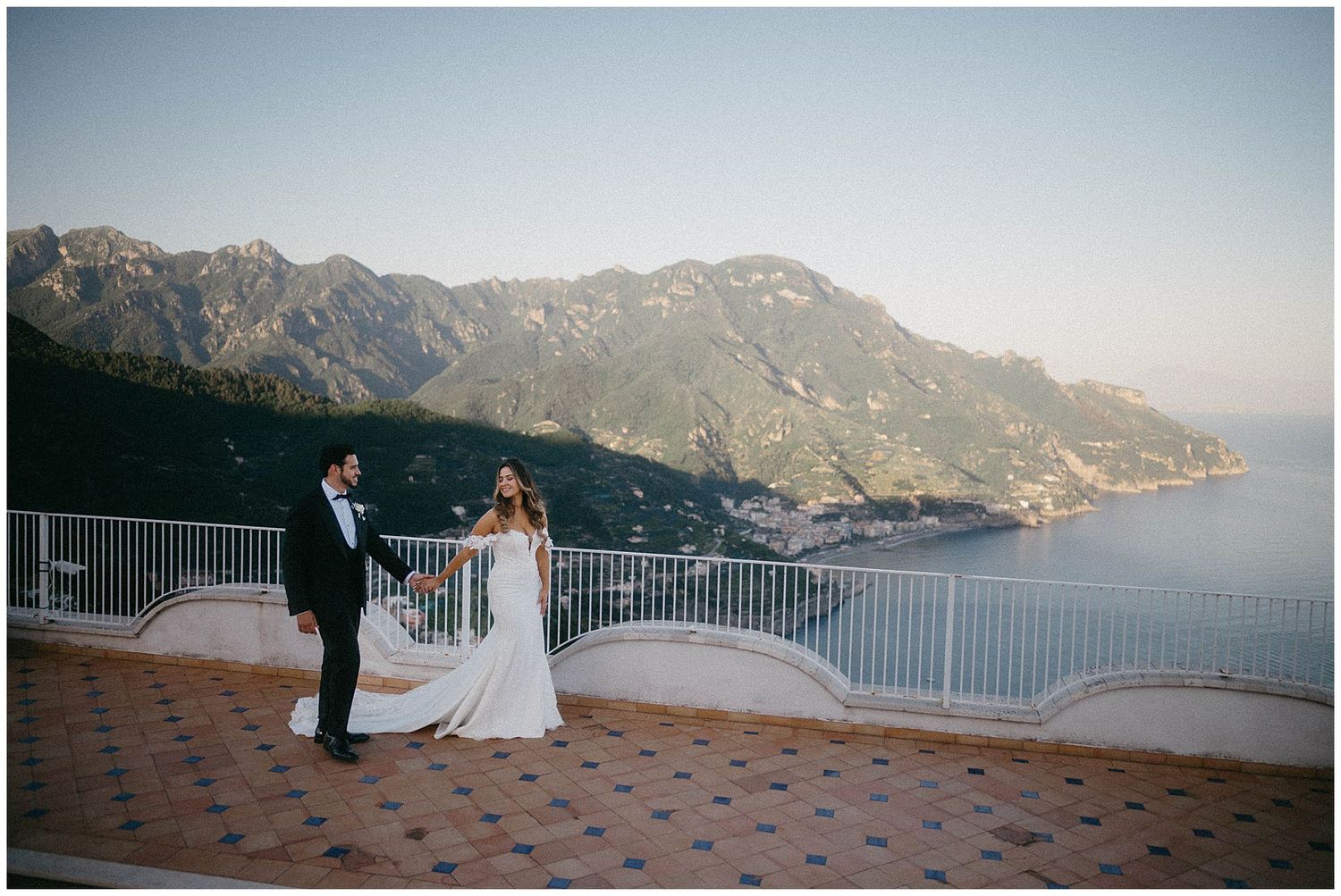 Two people share a romantic moment on a terrace overlooking the scenic Amalfi Coast mountains and Mediterranean Sea.