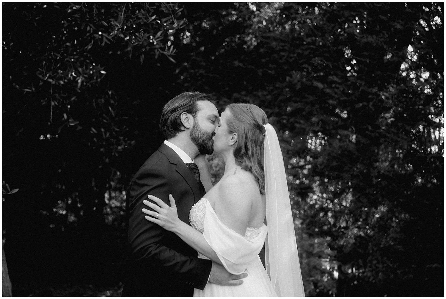 A romantic black and white wedding photo showing a couple sharing an intimate moment outdoors.