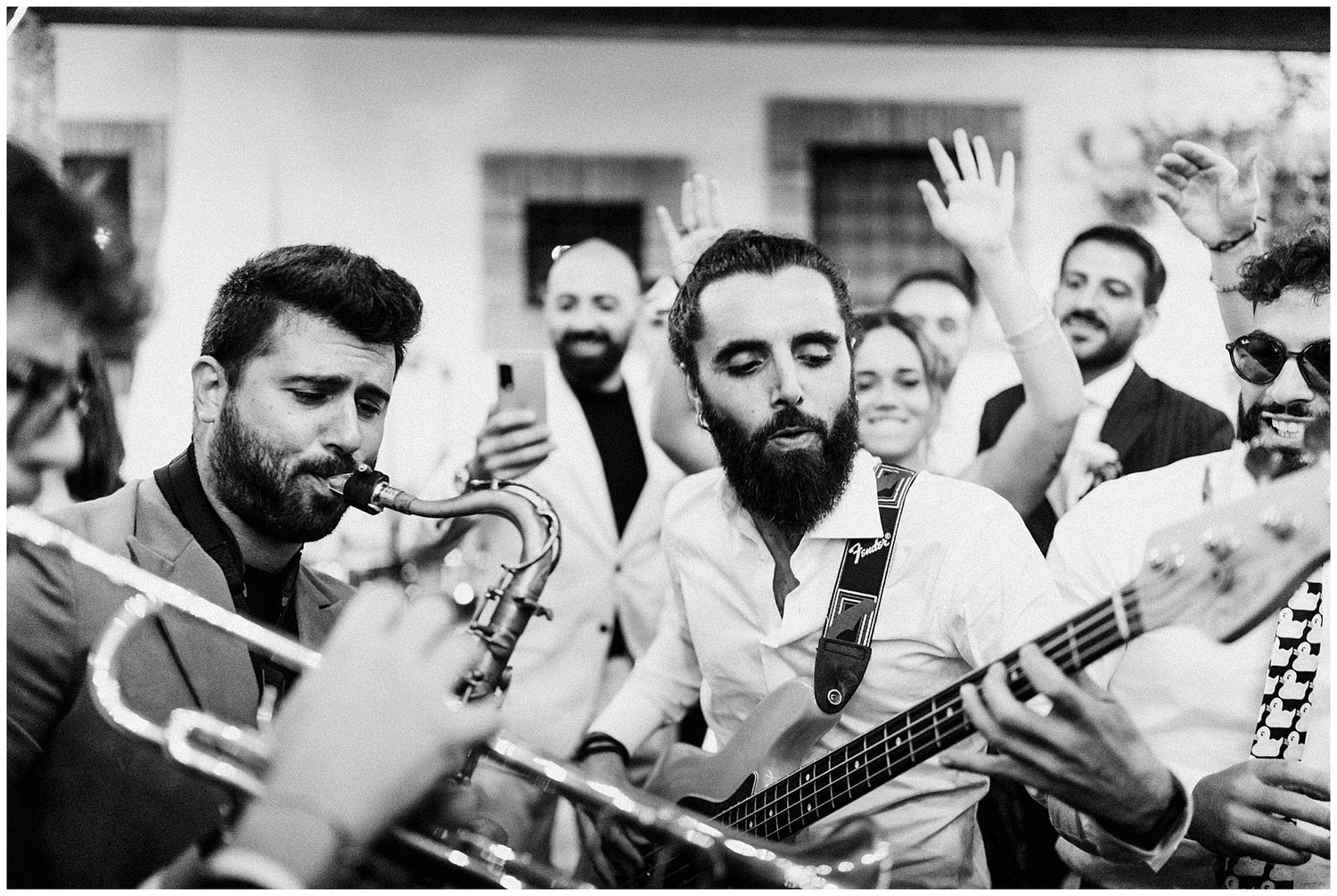 Musicians playing trumpet and guitar perform at an outdoor wedding celebration with guests in background.