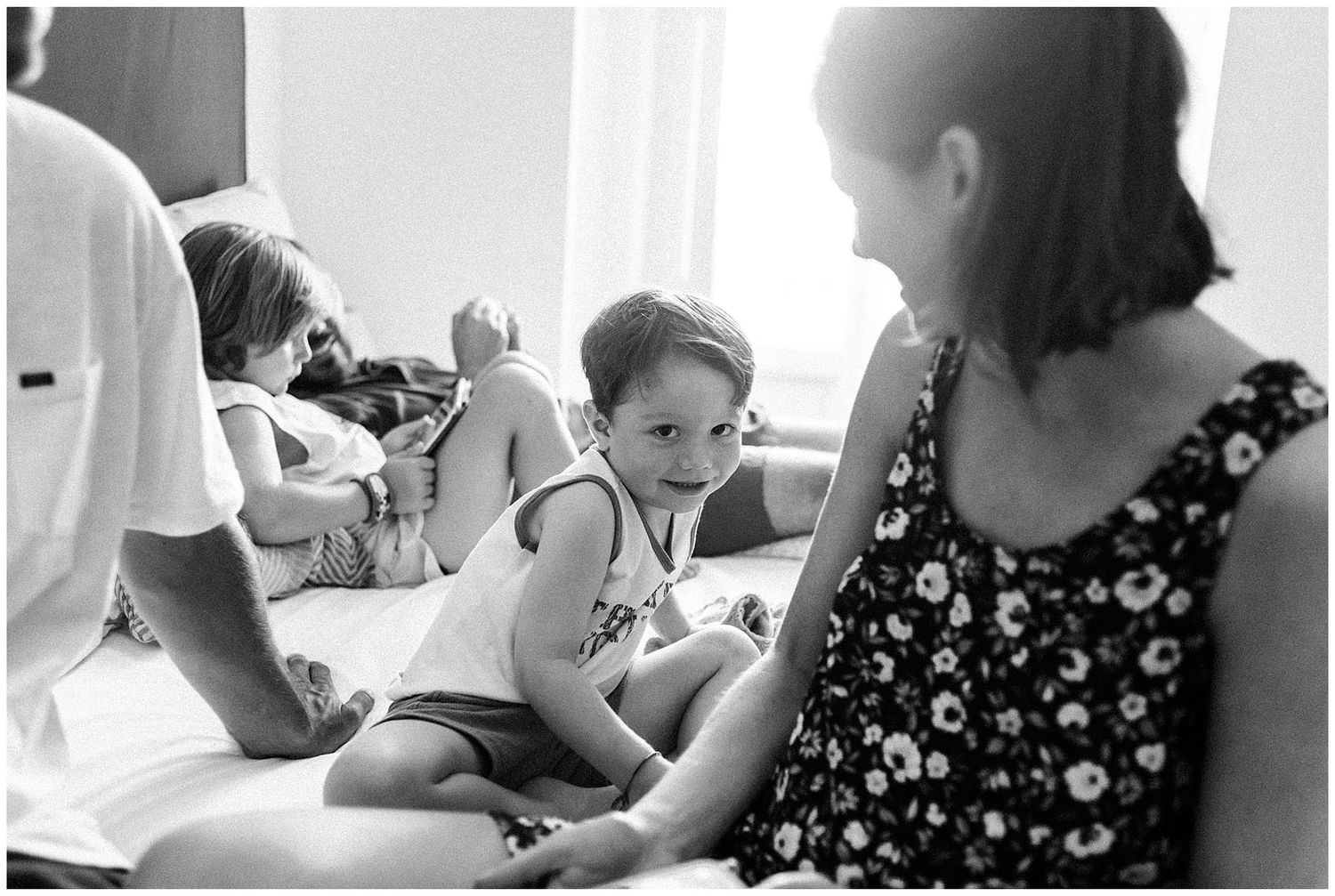 Black and white candid photograph showing people relaxing together in a casual indoor setting.