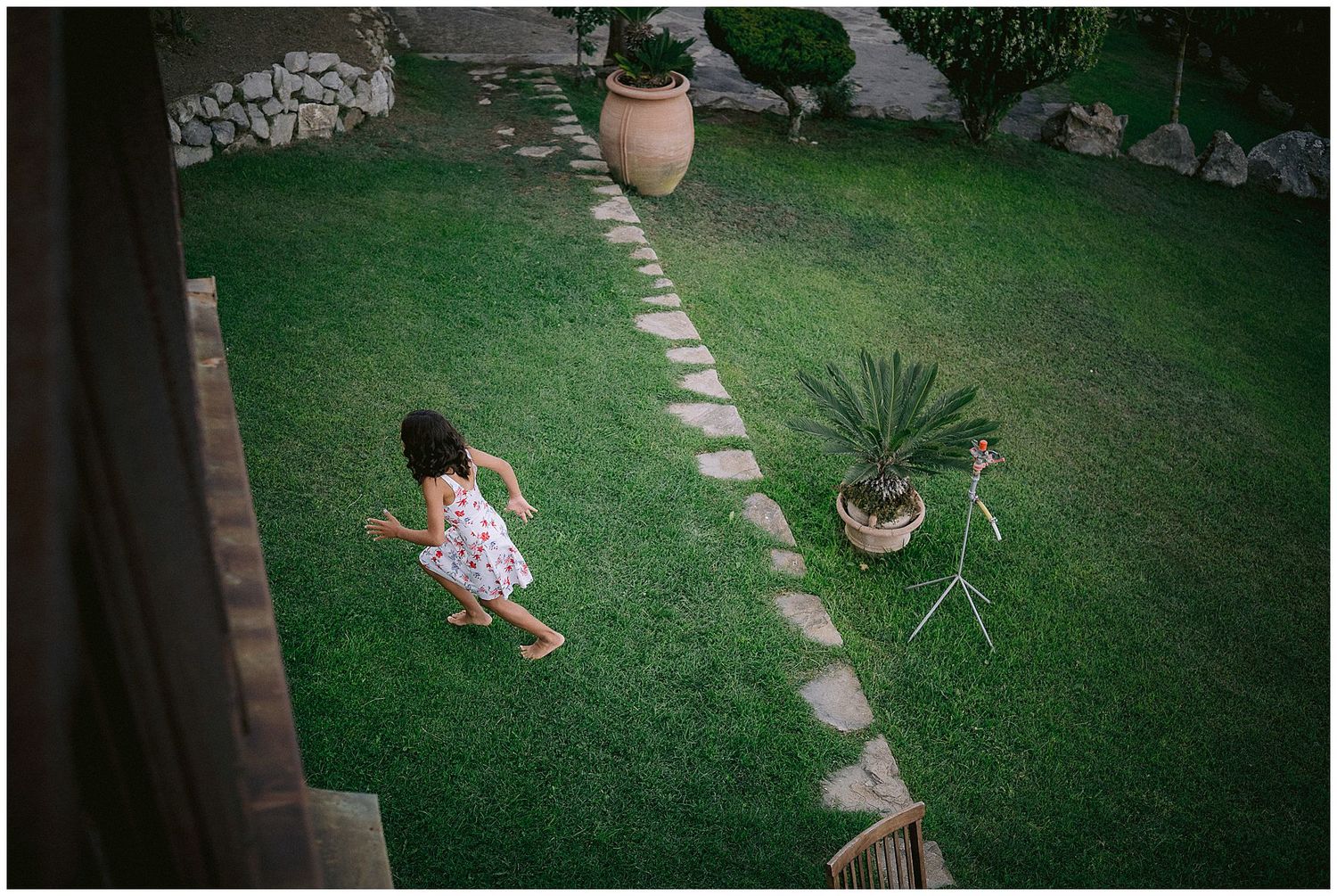 Overhead view of a well-maintained backyard garden with stone pathway and potted plants on green lawn.