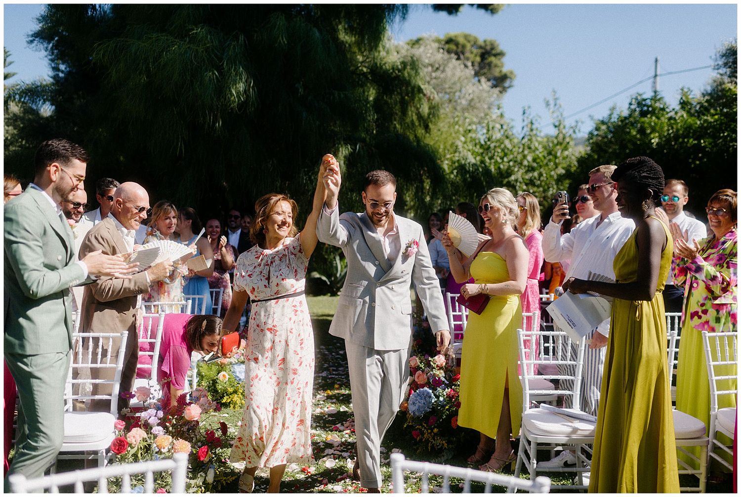 Wedding guests raise their glasses in celebration during an outdoor garden party reception.