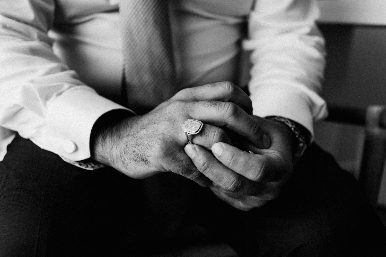 A black and white close-up shot of clasped hands with a ring, showing contemplative body language.
