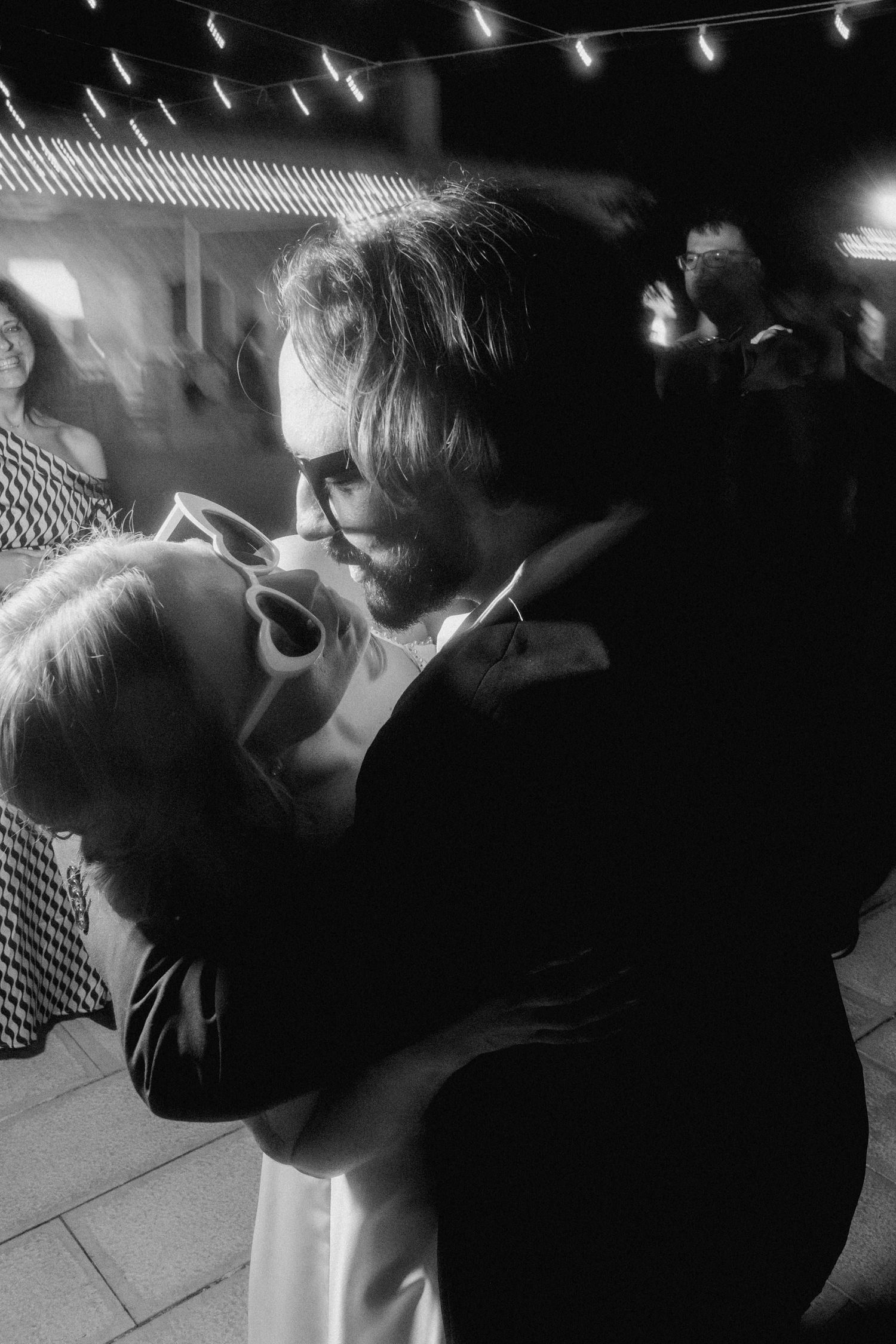 A romantic couple shares an intimate dance moment under twinkling lights at night.