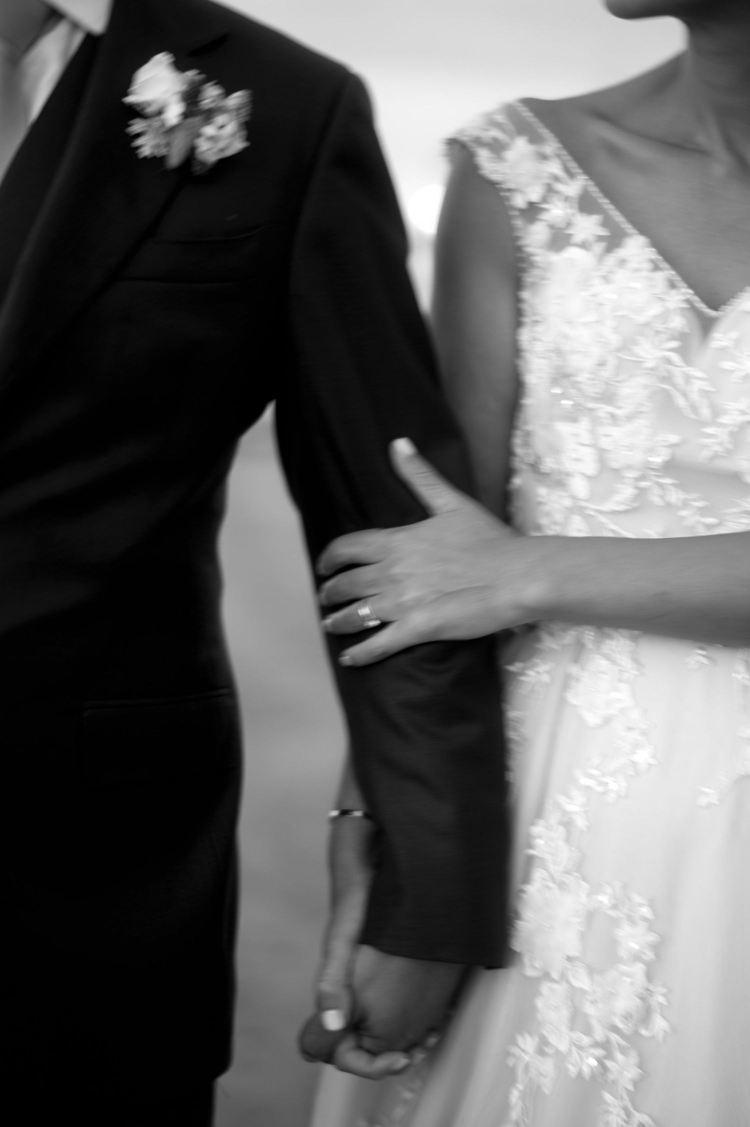 A close-up black and white photo shows a couple in formal wedding attire with bride's hand on groom's arm.