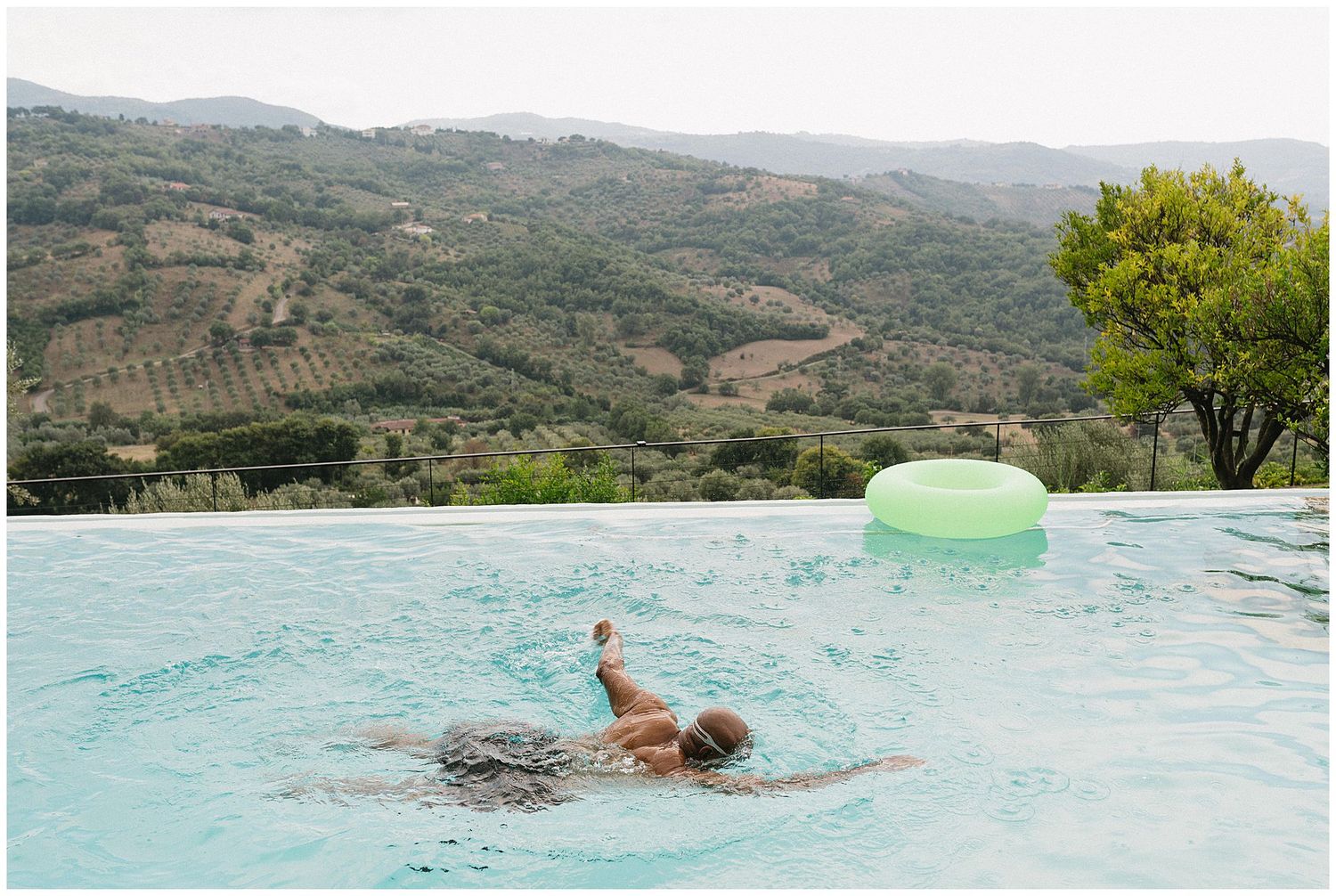 Someone swimming in a stunning infinity pool overlooking terraced hills and countryside in a scenic mountain landscape.