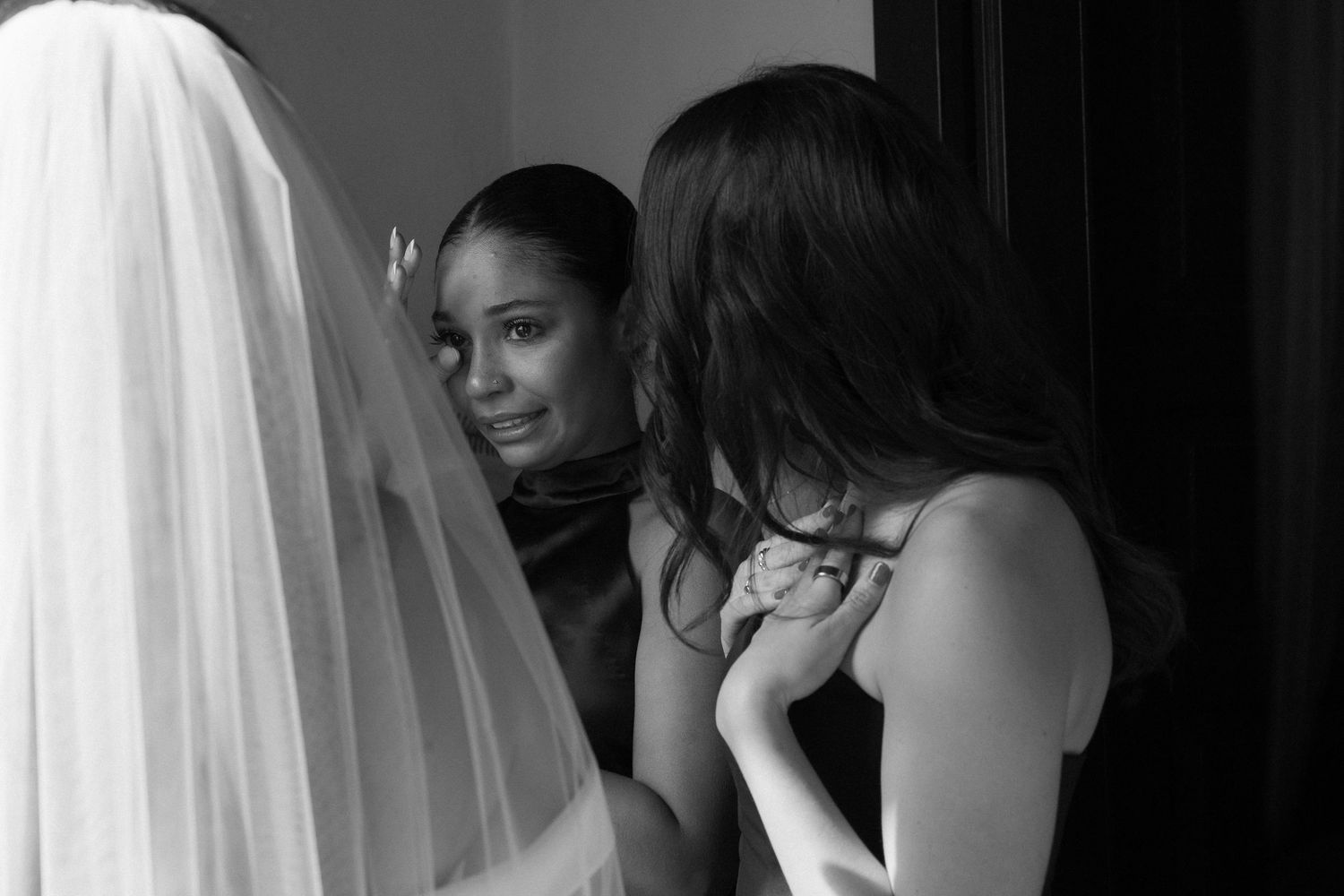 Candid black and white photo of bridesmaids helping bride with veil.
