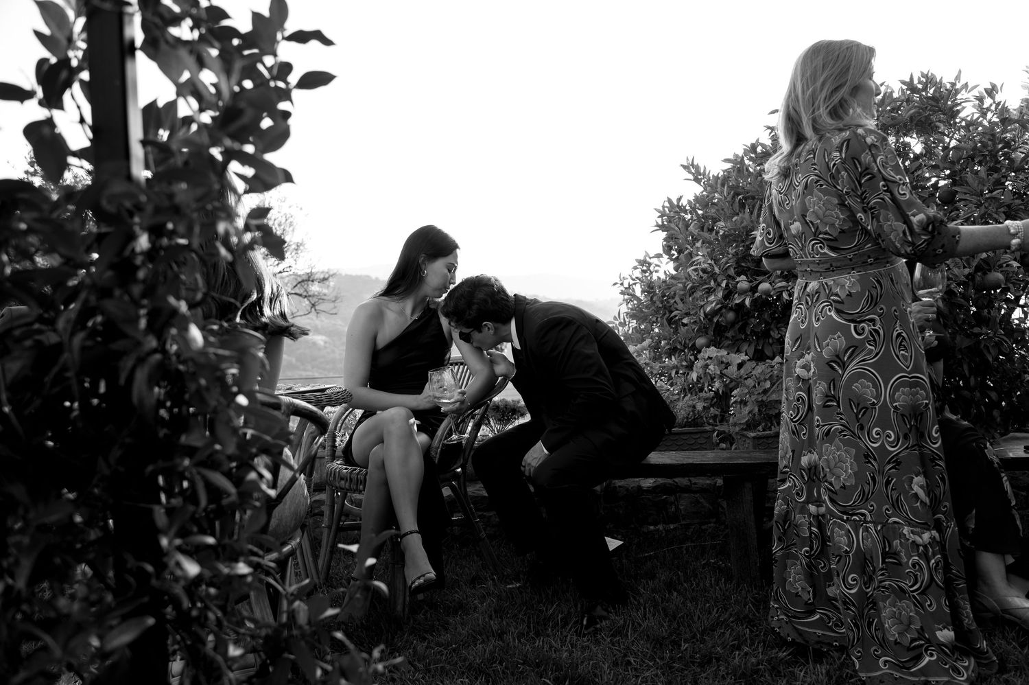 Two people share an intimate moment on a bench in a garden setting with lush greenery.