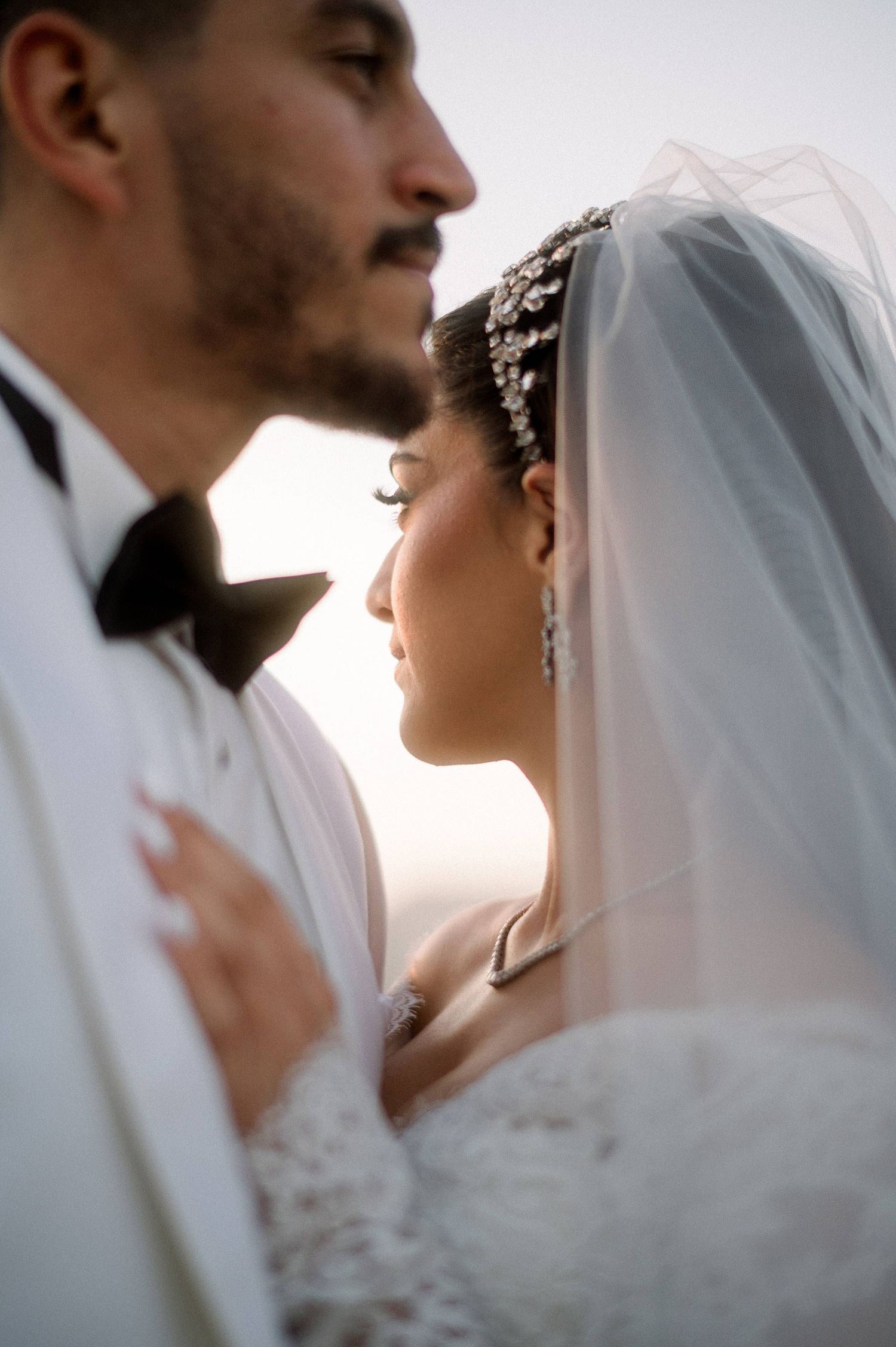 Romantic close-up of newlyweds sharing an intimate moment in white wedding attire against soft light.