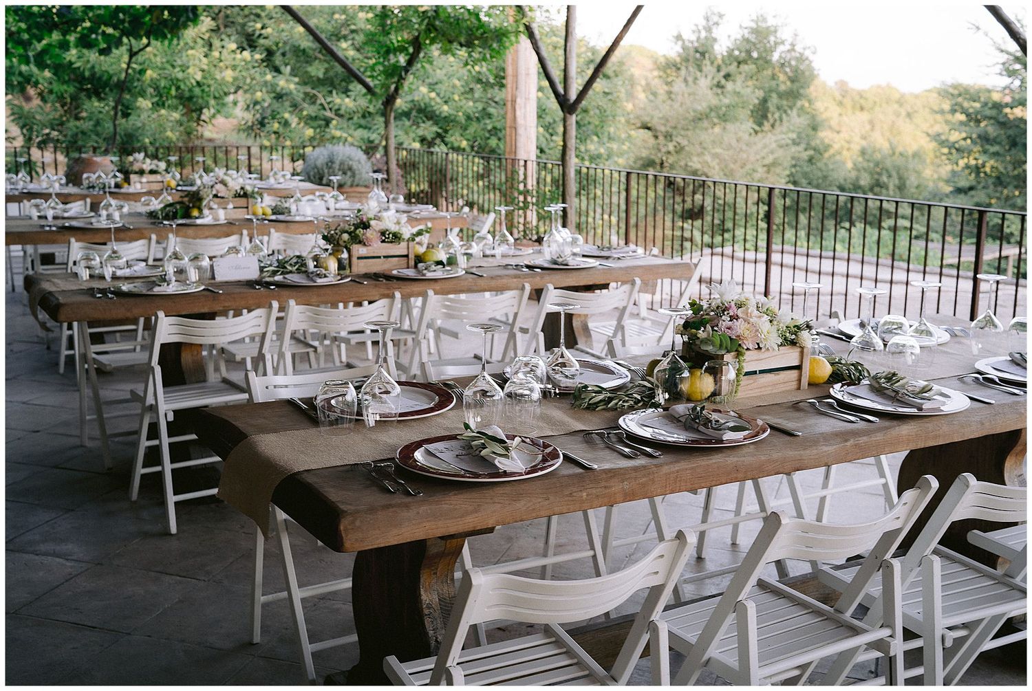 Rustic wooden tables set for an elegant outdoor wedding reception with white folding chairs and place settings.