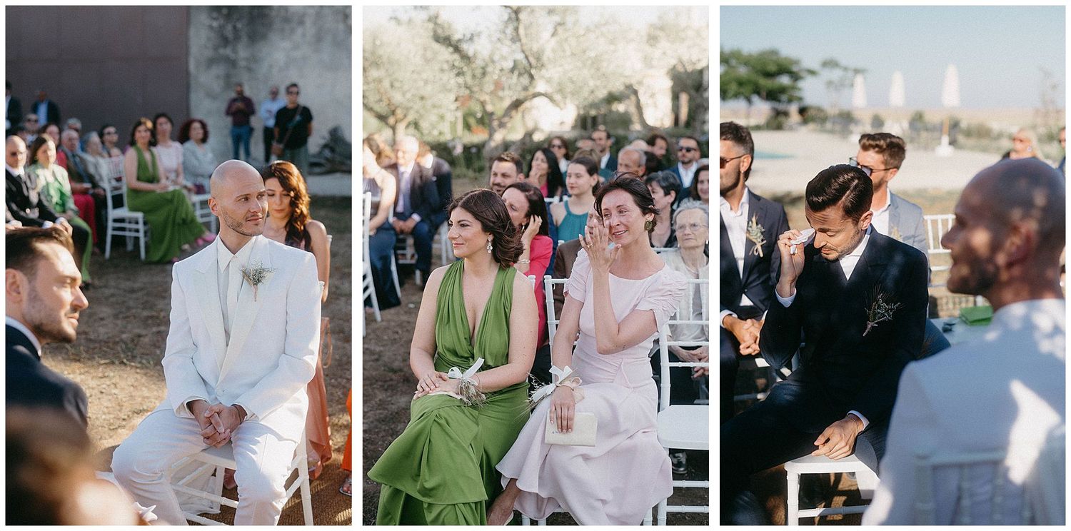Joyful guests attend an outdoor wedding ceremony seated in white chairs against a rustic backdrop.
