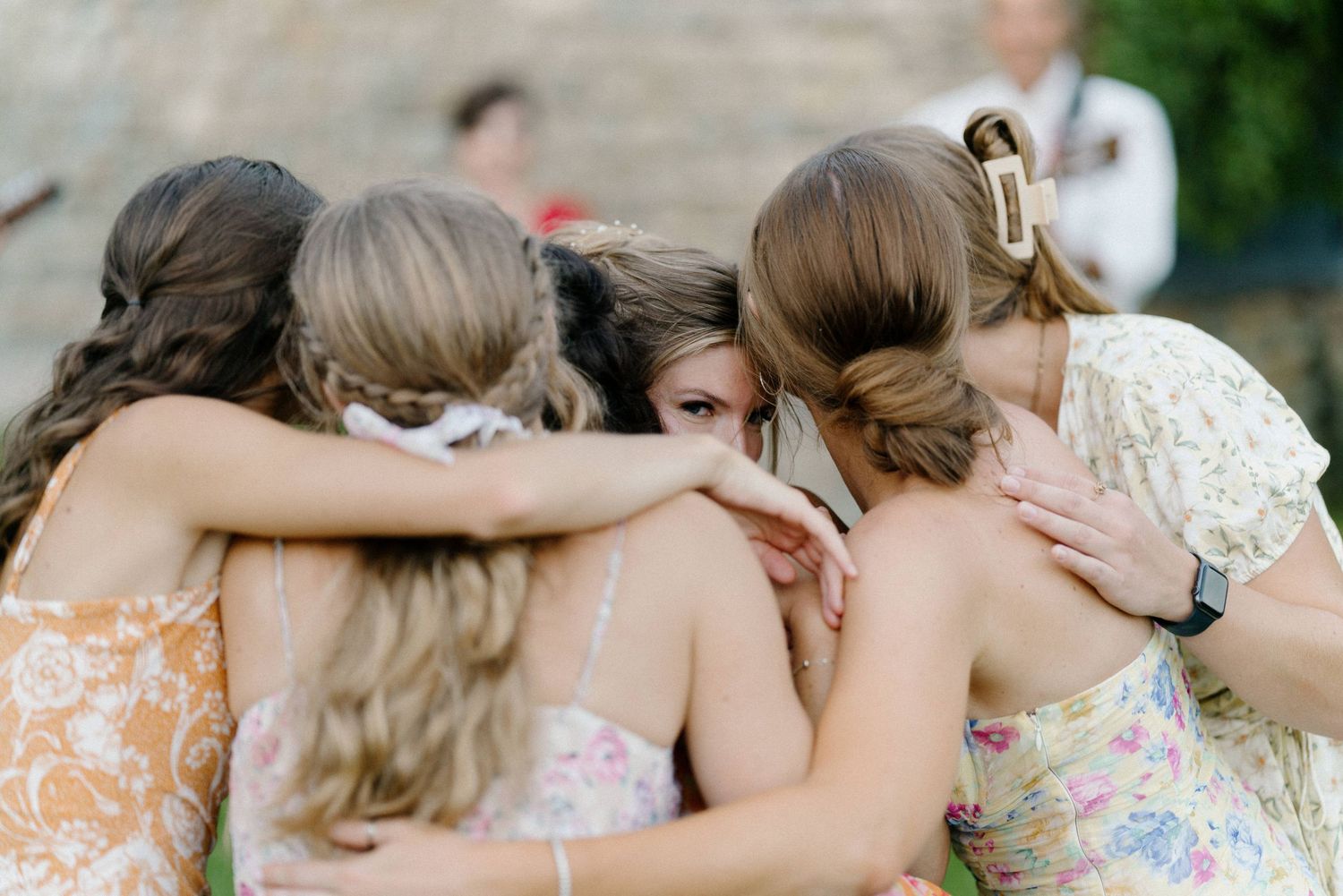 A group of friends huddled together in floral dresses at an outdoor event.