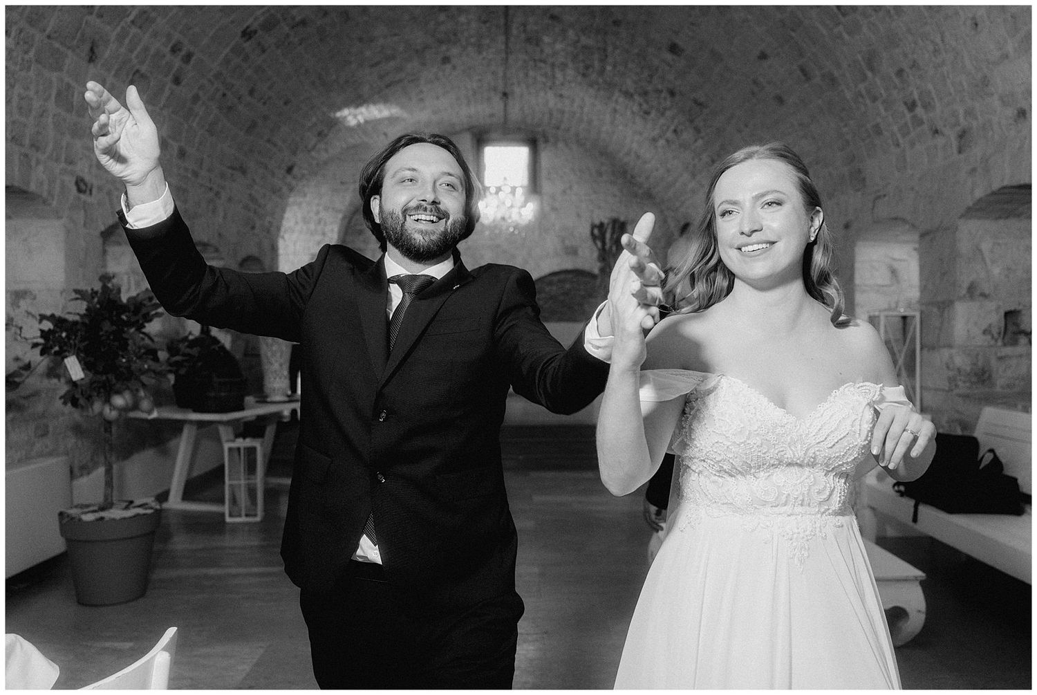 A black and white photo of a joyful wedding reception with a couple celebrating on the dance floor.