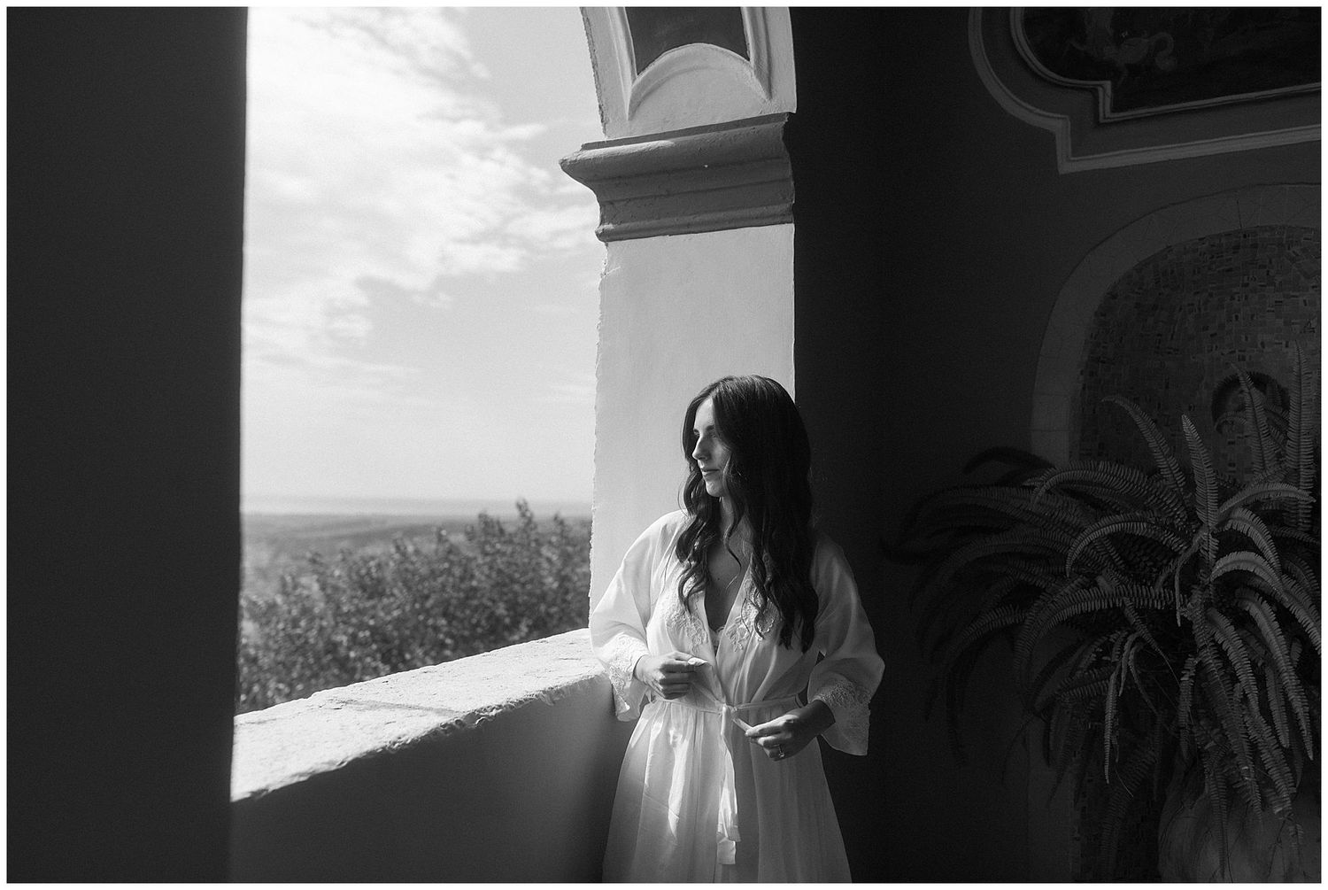 A woman in a white dress stands by a window in a classic architectural setting.