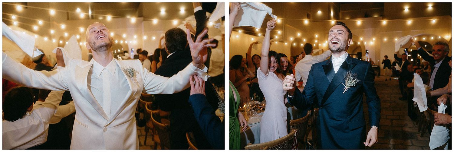 Wedding party celebrates on dance floor under string lights as couple dances joyfully at indoor reception venue.