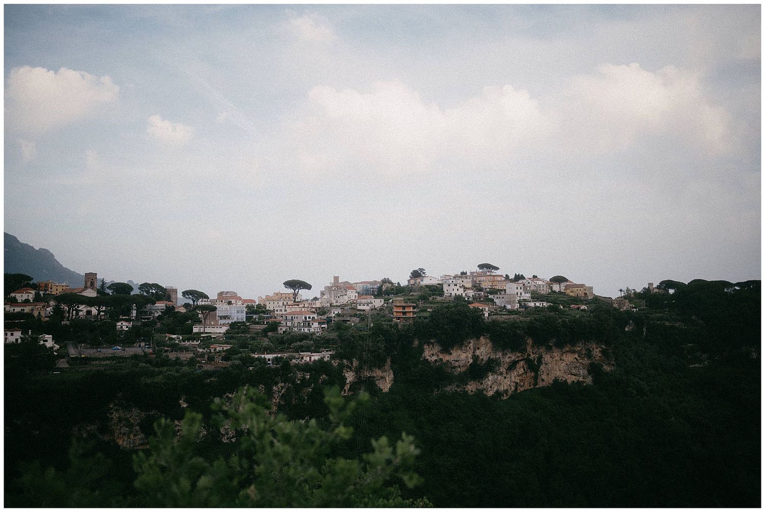 Hillside Mediterranean village with white buildings perched on rocky cliffs against cloudy sky.