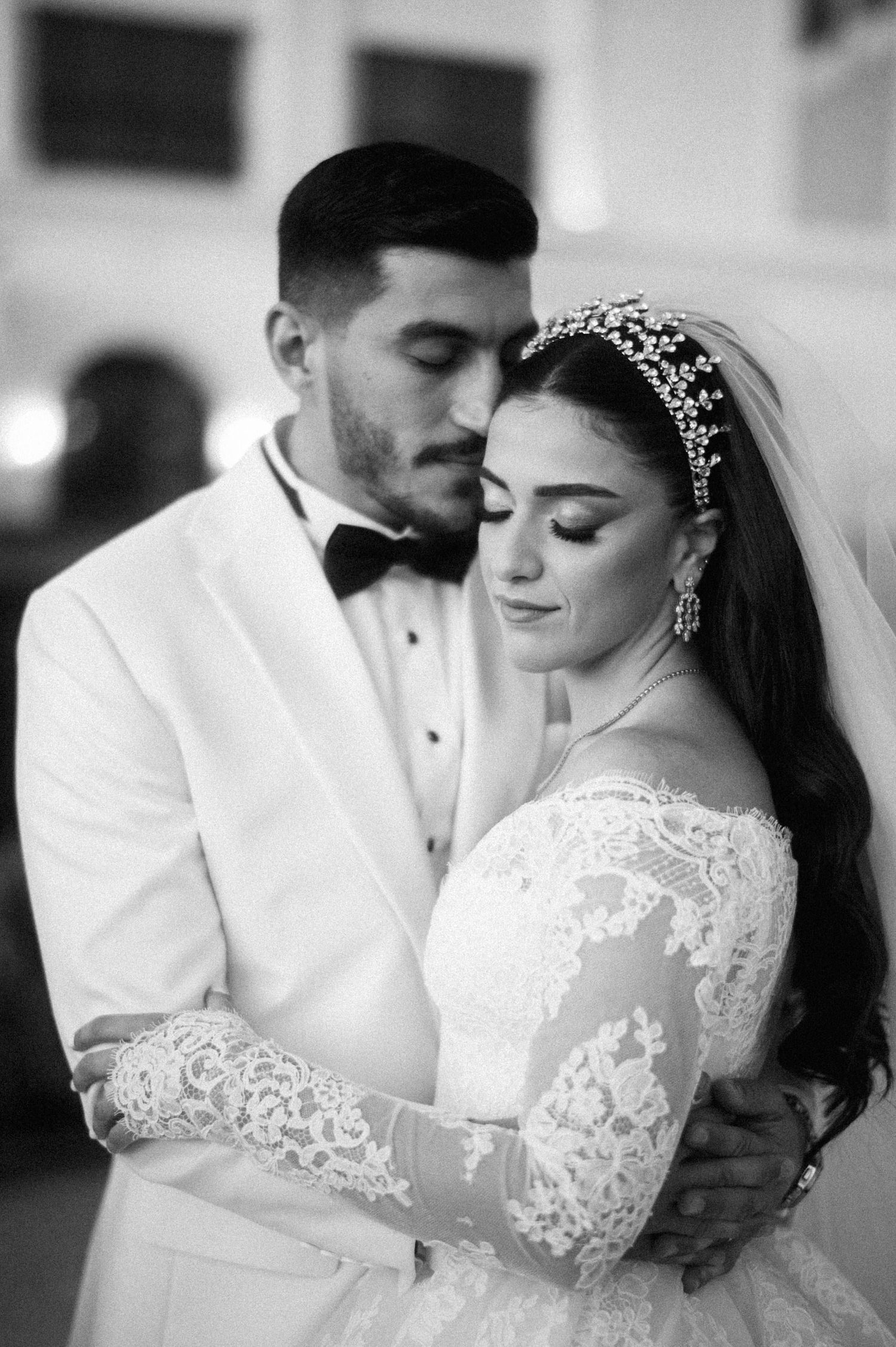 A romantic black and white wedding portrait of a bride and groom embracing, with lace details and crystal headpiece.