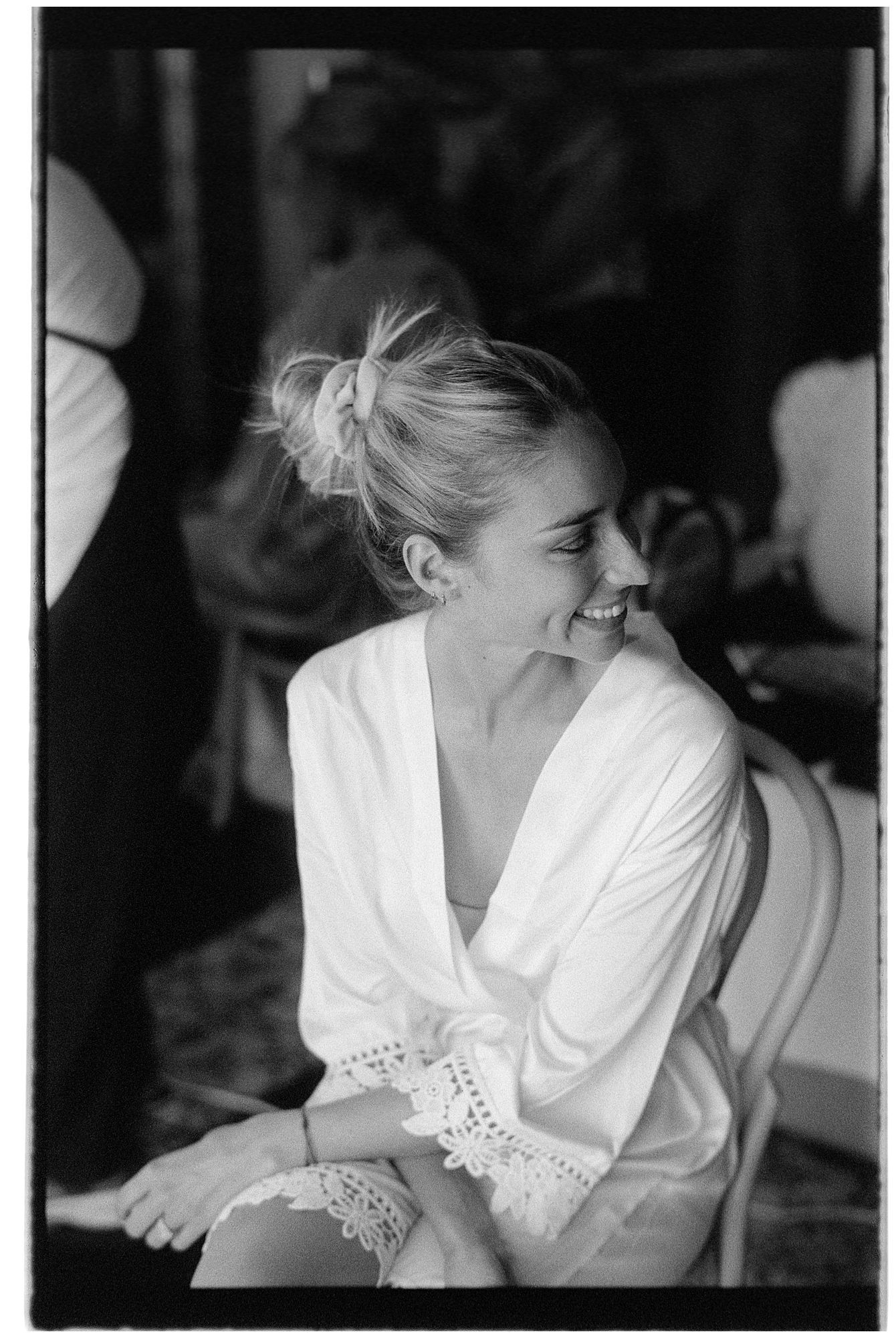 Black and white photograph of someone in a white lace-trimmed robe smiling with hair pulled back in a bun.