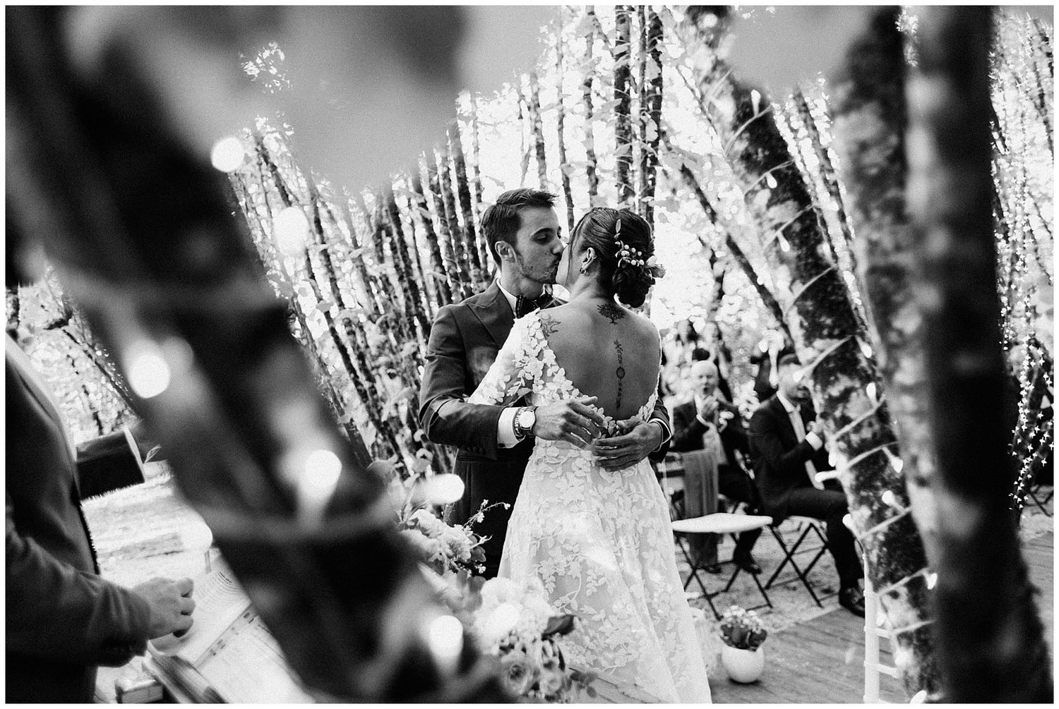 Black and white photo of a couple dancing between decorative birch branches at a wedding reception.