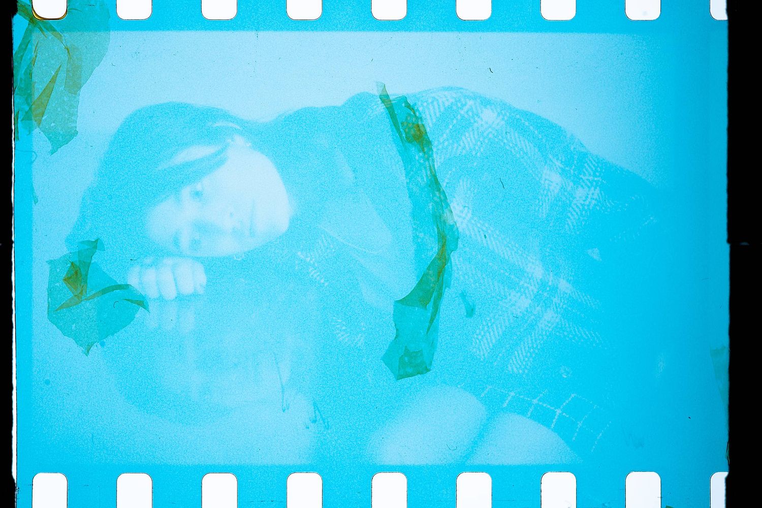 Overlapping blue tinted film negatives with sprocket holes creating an ethereal double exposure effect.