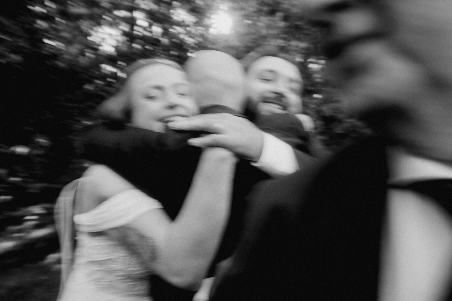 A blurred black and white candid photo showing a joyful group embrace at what appears to be an outdoor event.
