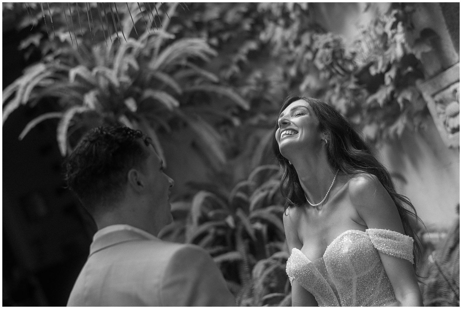 Black and white candid moment of intimate laughter shared between a couple at a romantic outdoor garden setting.