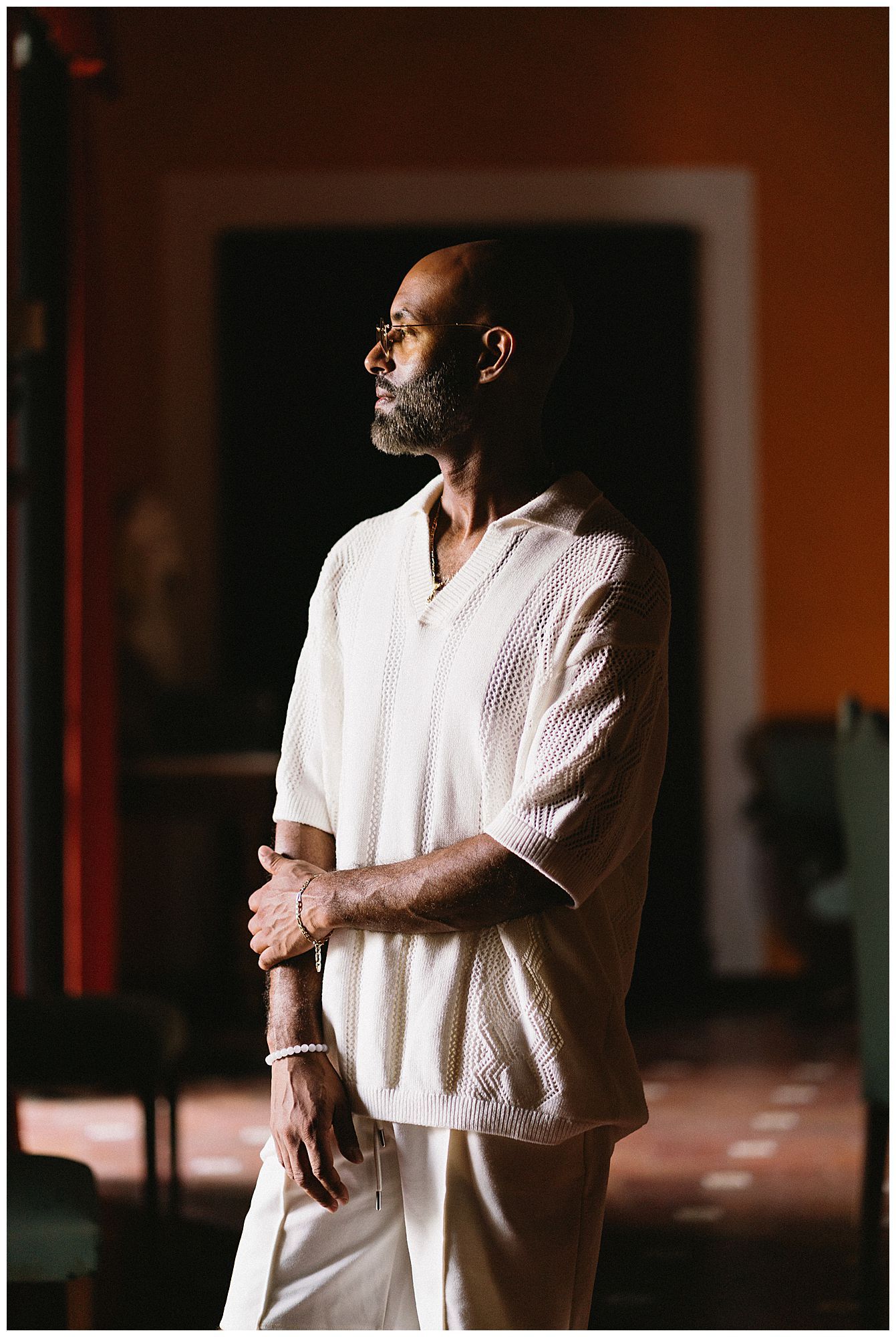 Artistic portrait of person in white clothing standing in dramatic side lighting with dark background.