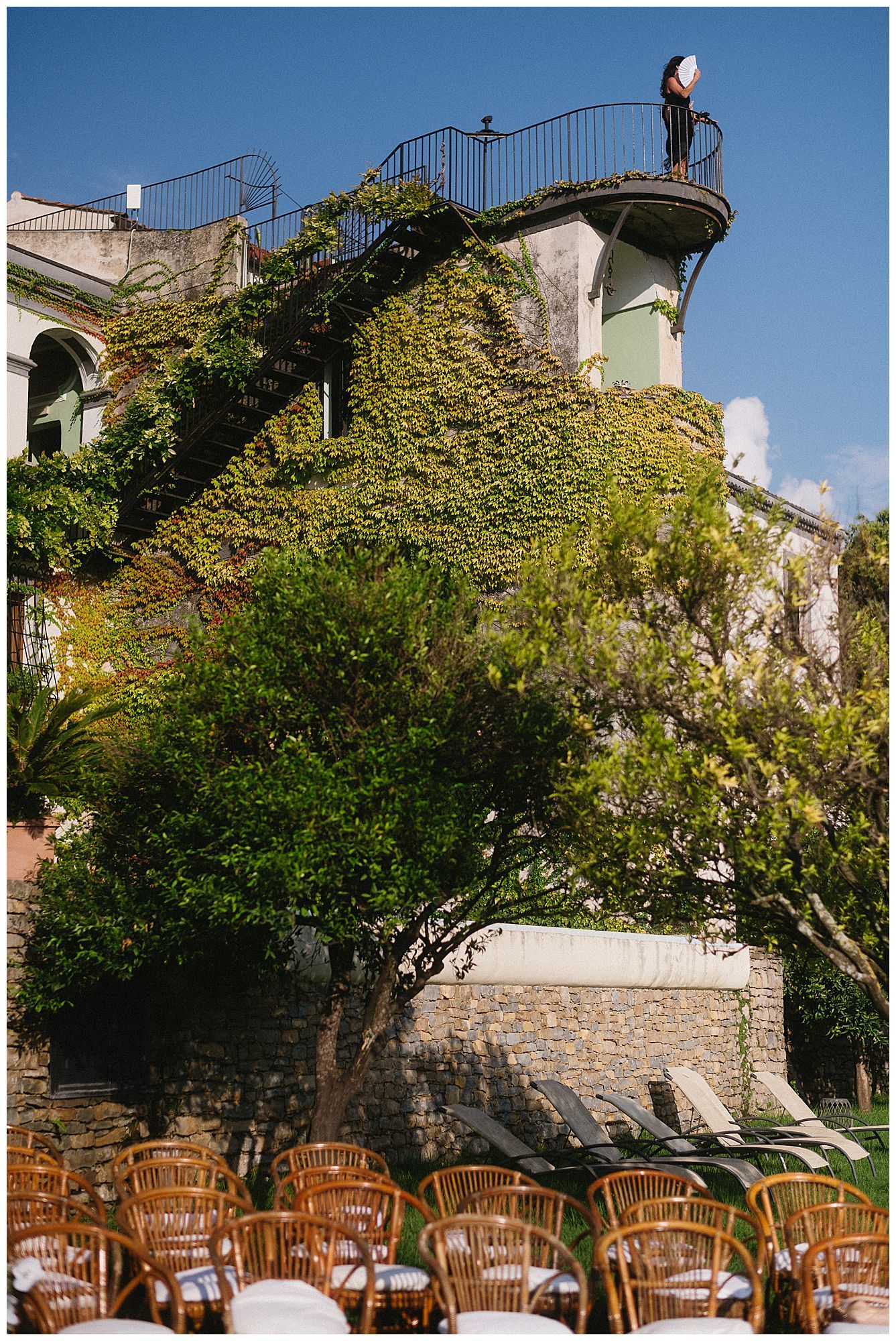 Ivy-covered building with wicker chairs below and a curved stone staircase leading to an observation deck against blue sky.