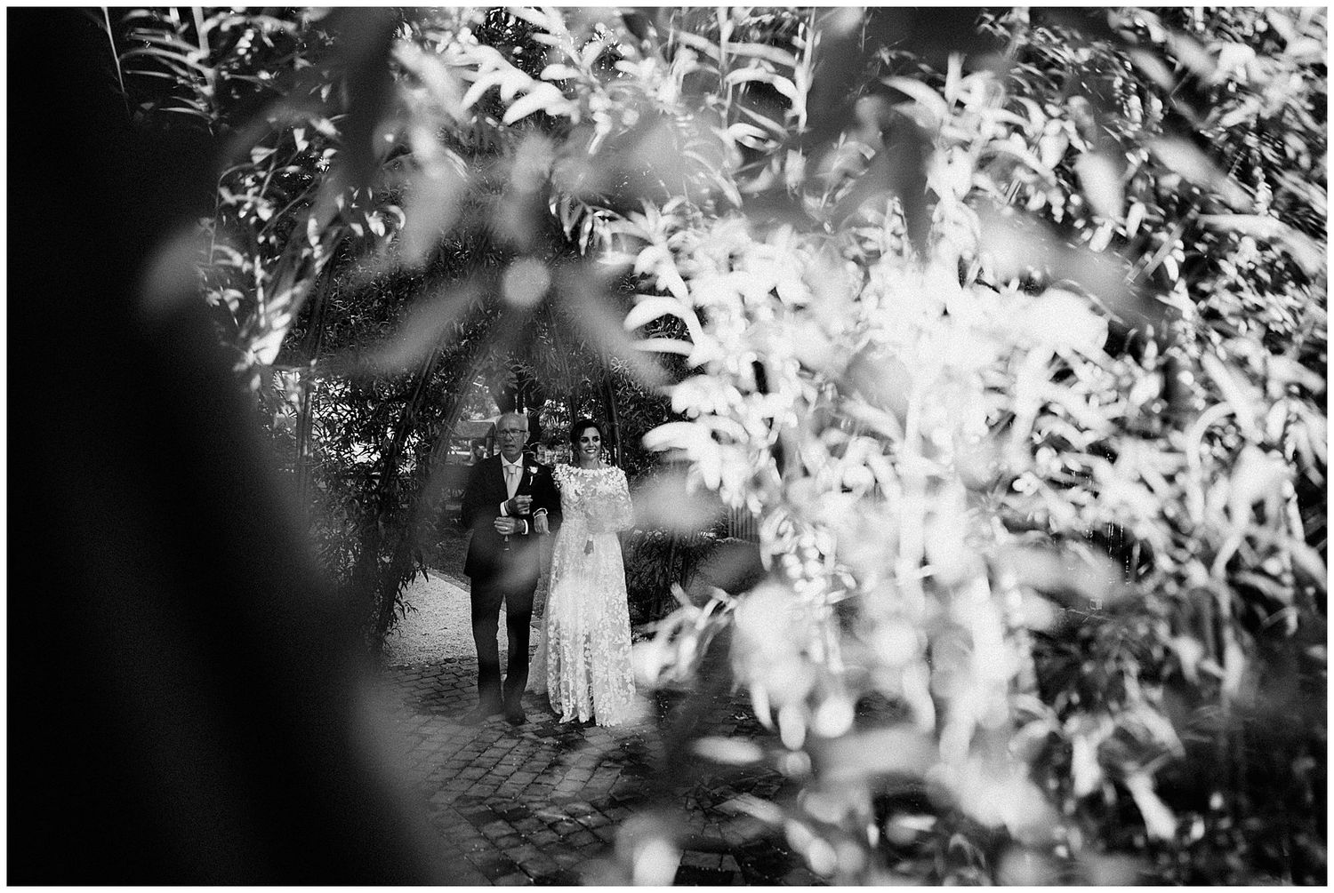 A black and white artistic wedding photograph showing silhouettes through dreamy foliage and bokeh effects.