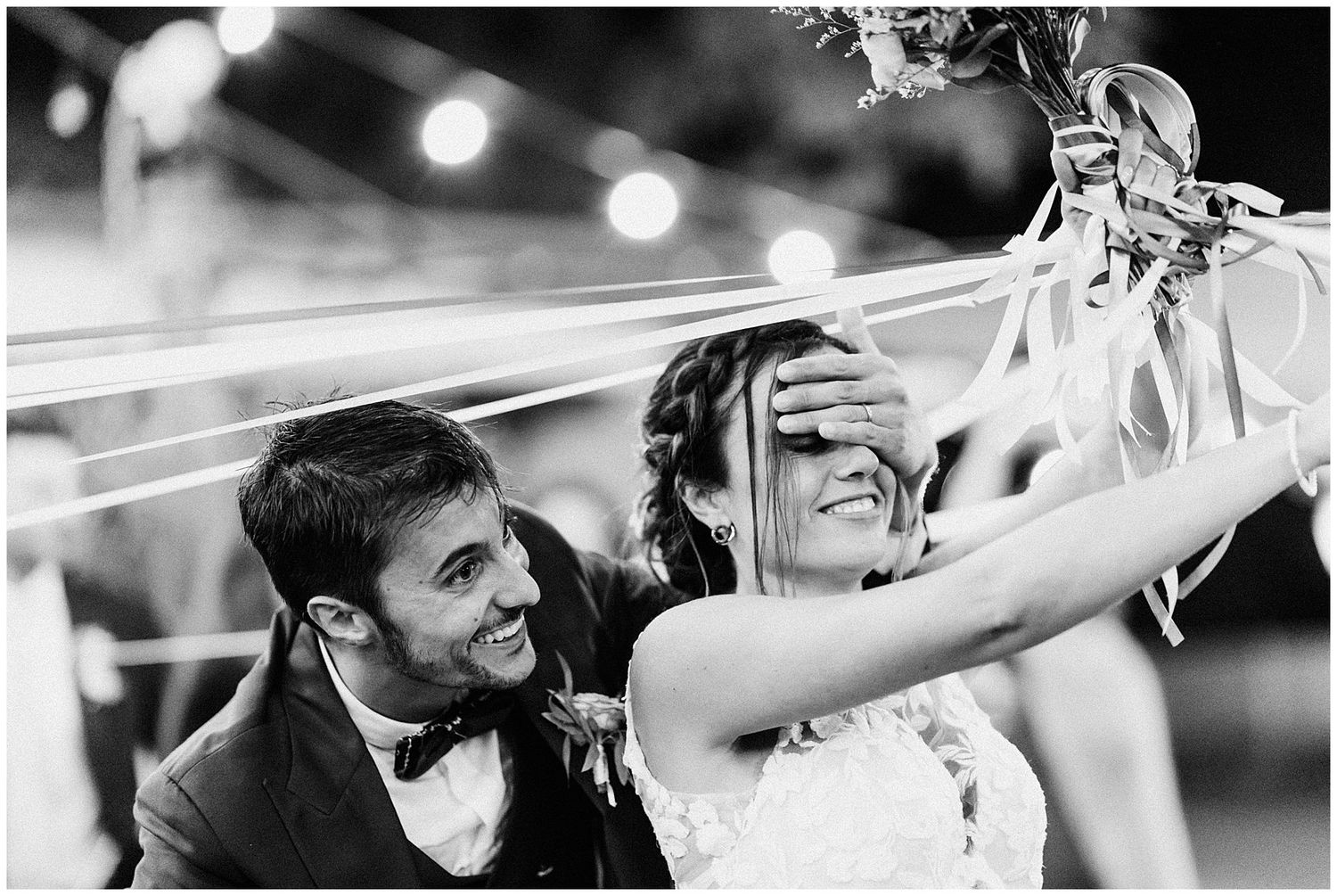 Wedding couple and guests laughing during candid indoor reception moments under soft lighting.