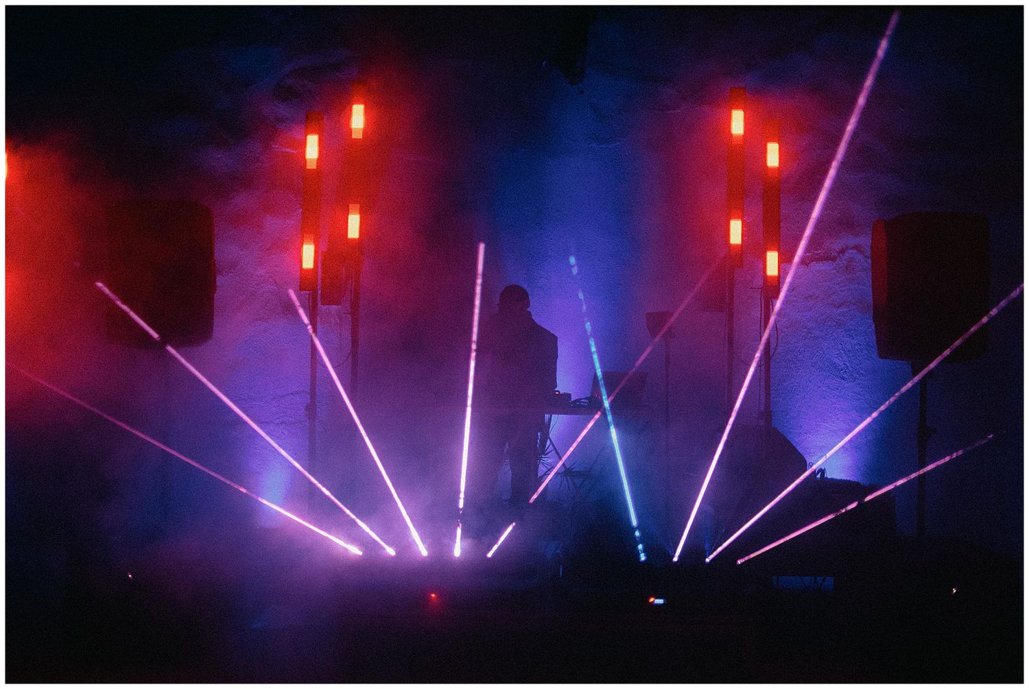Colorful laser light show with red and blue beams illuminating a dark stage during a concert performance.